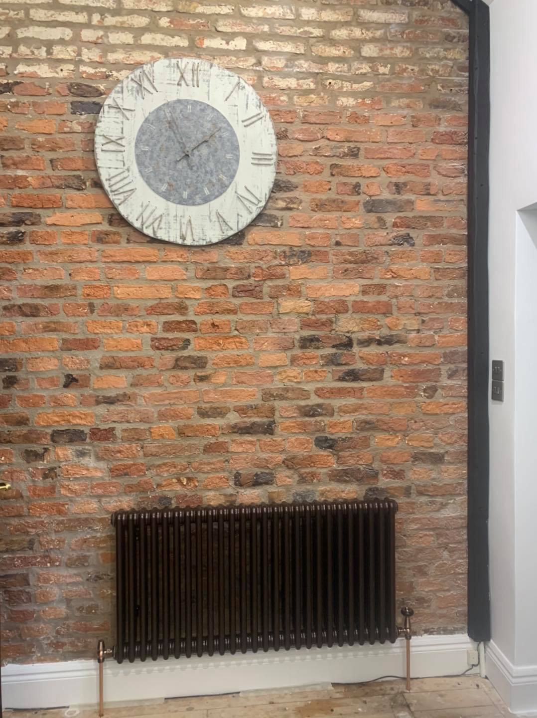 Brick wall with a large clock and a dark radiator.