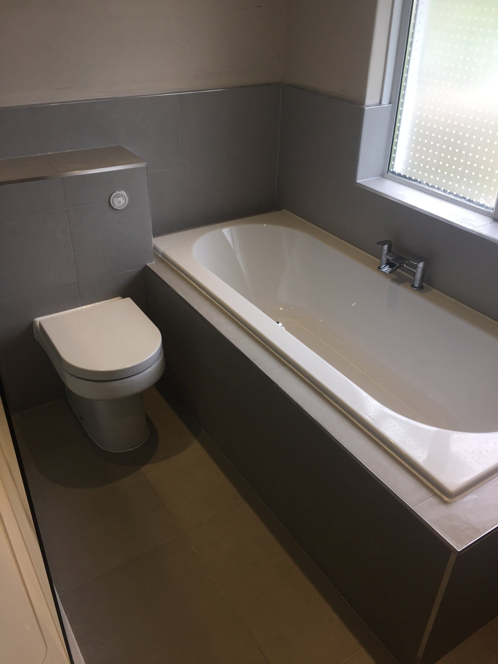 Bathroom with gray walls, built-in bathtub, and toilet; window with frosted glass.