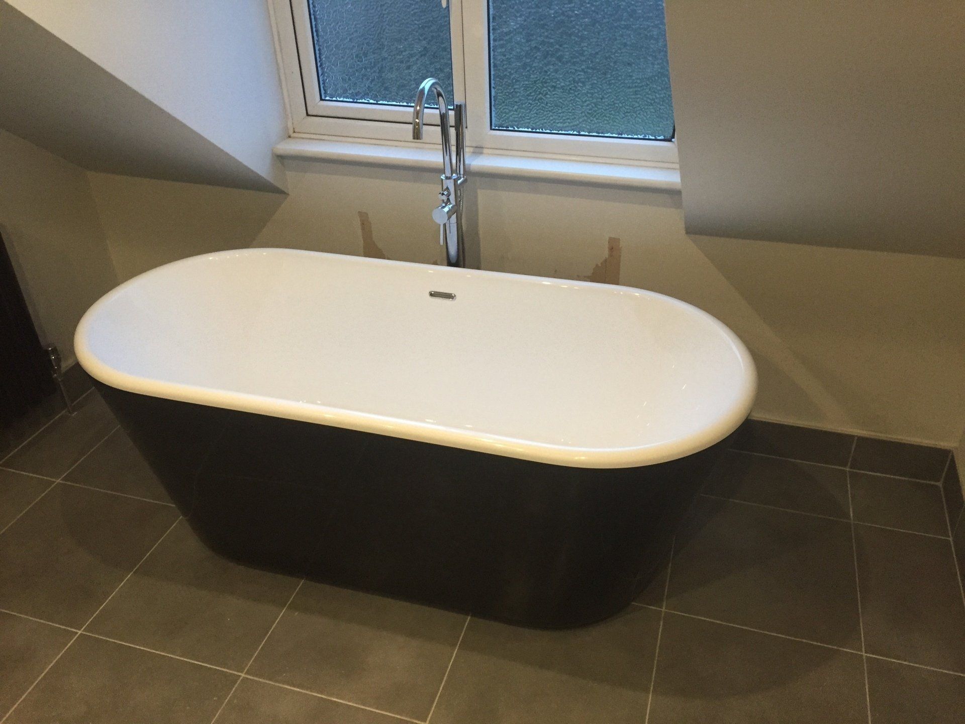 Oval bathtub, black exterior, white interior, near a window in a bathroom.