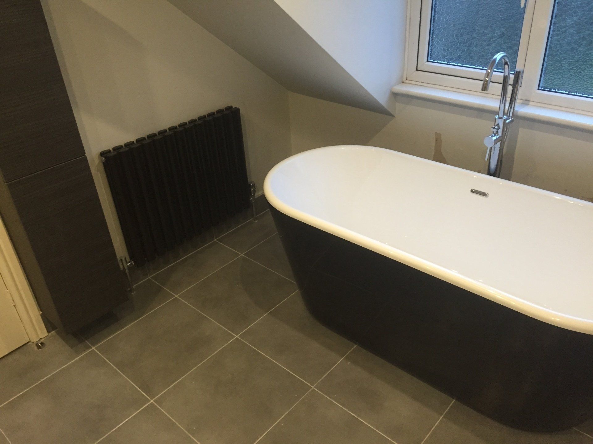 Bathroom with black freestanding tub, dark radiator, and gray tiled floor.