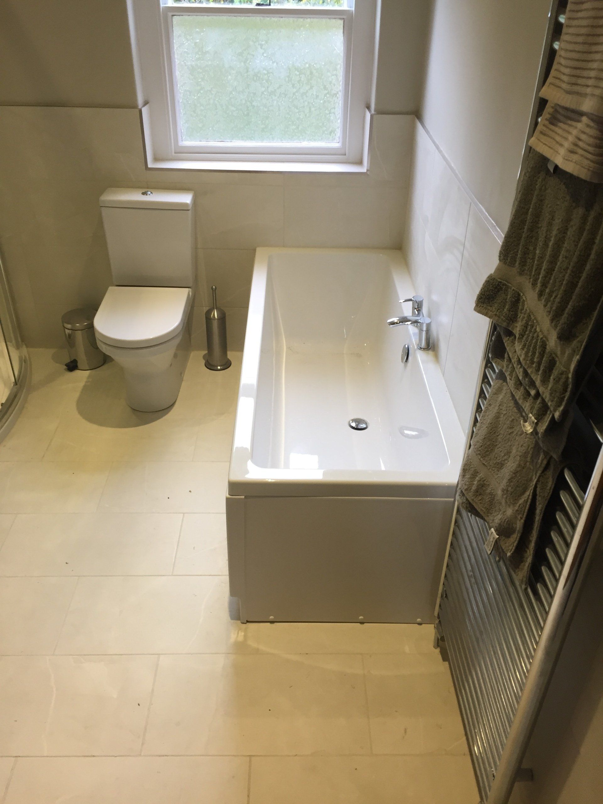 Bathroom with white toilet, bathtub, and neutral tiles. Towel rack on the right.