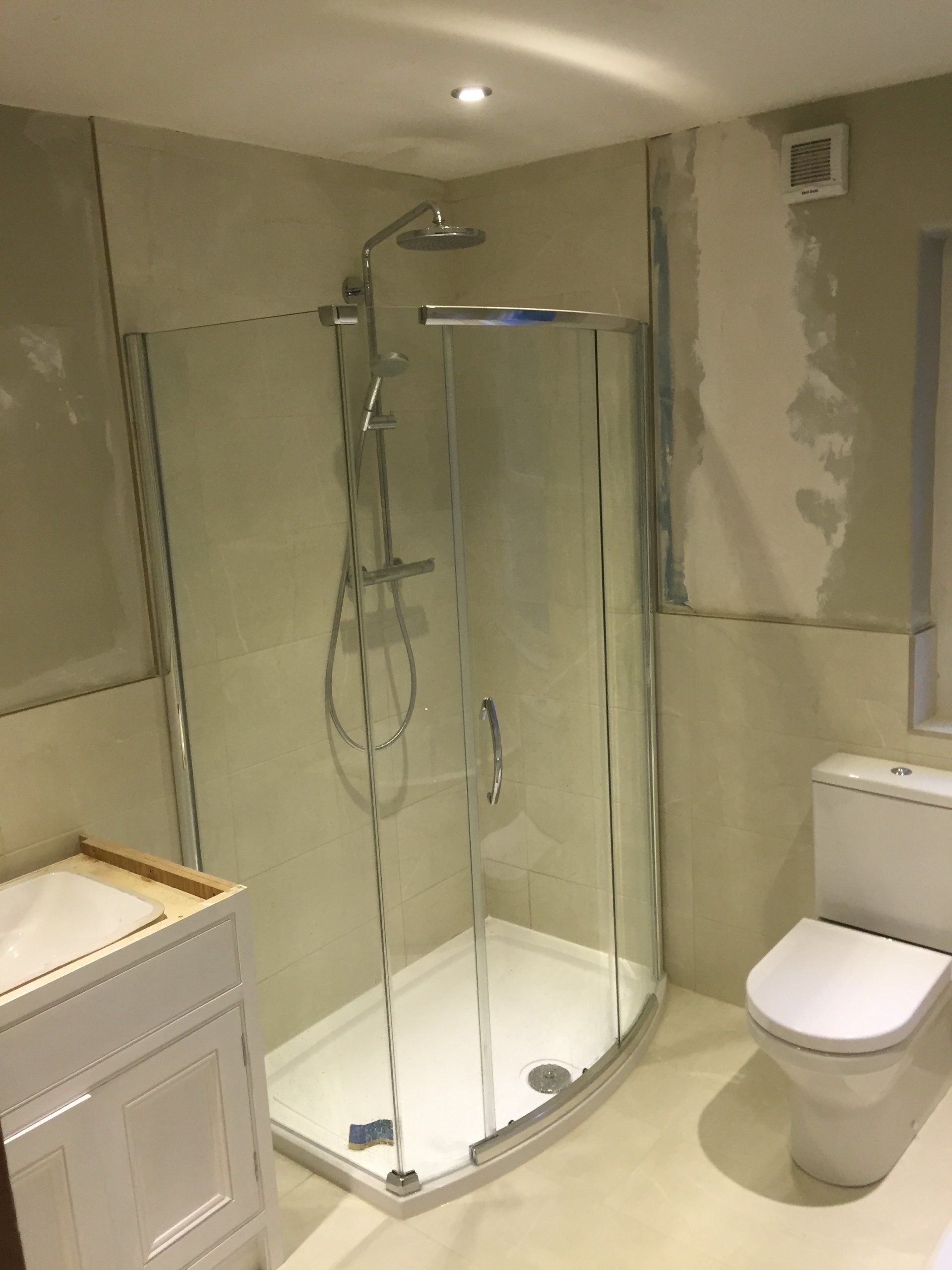 Bathroom renovation with a corner shower, toilet, and vanity. Beige and white tones.