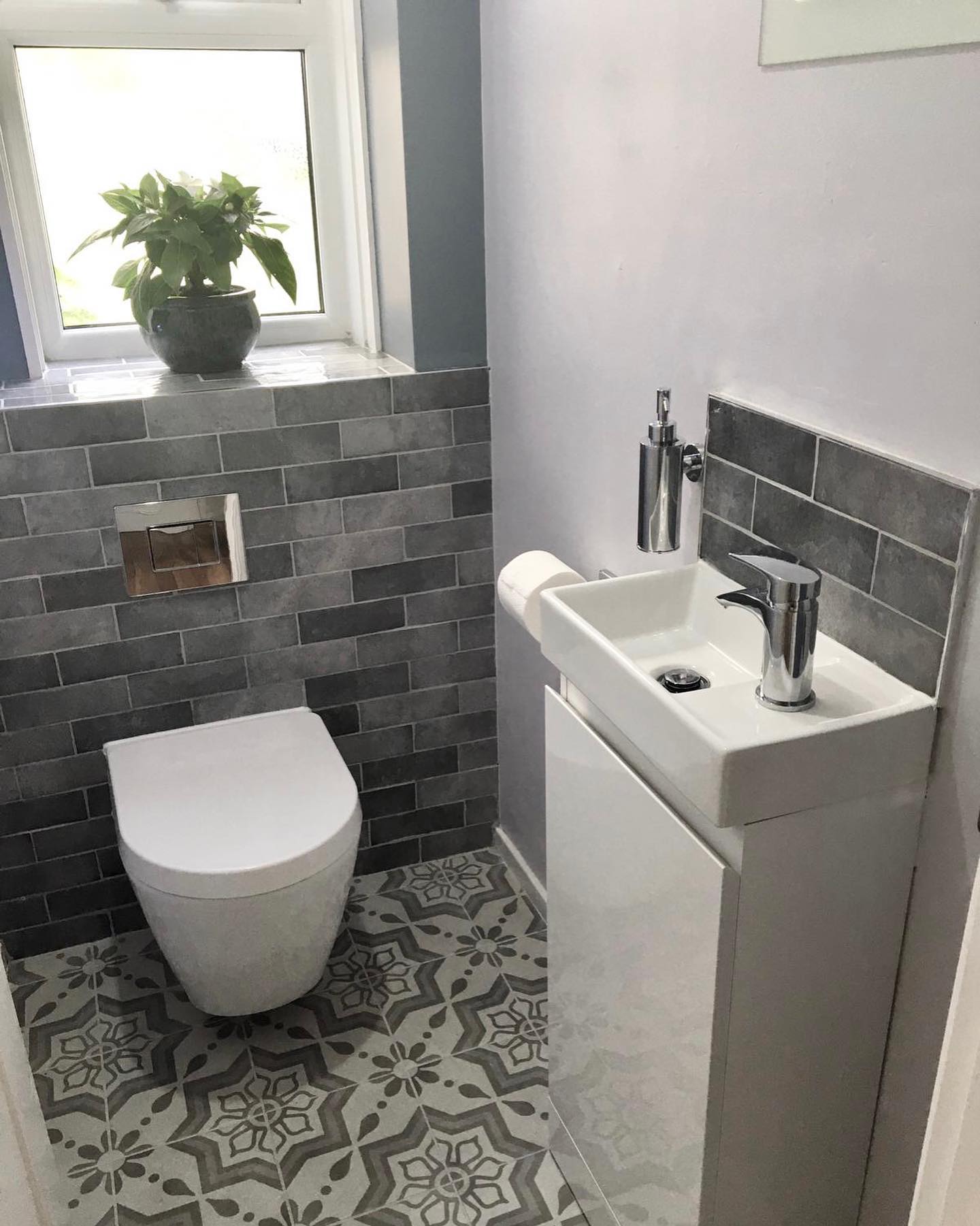 Small modern bathroom with gray tiled accent wall, white toilet and sink, patterned floor.