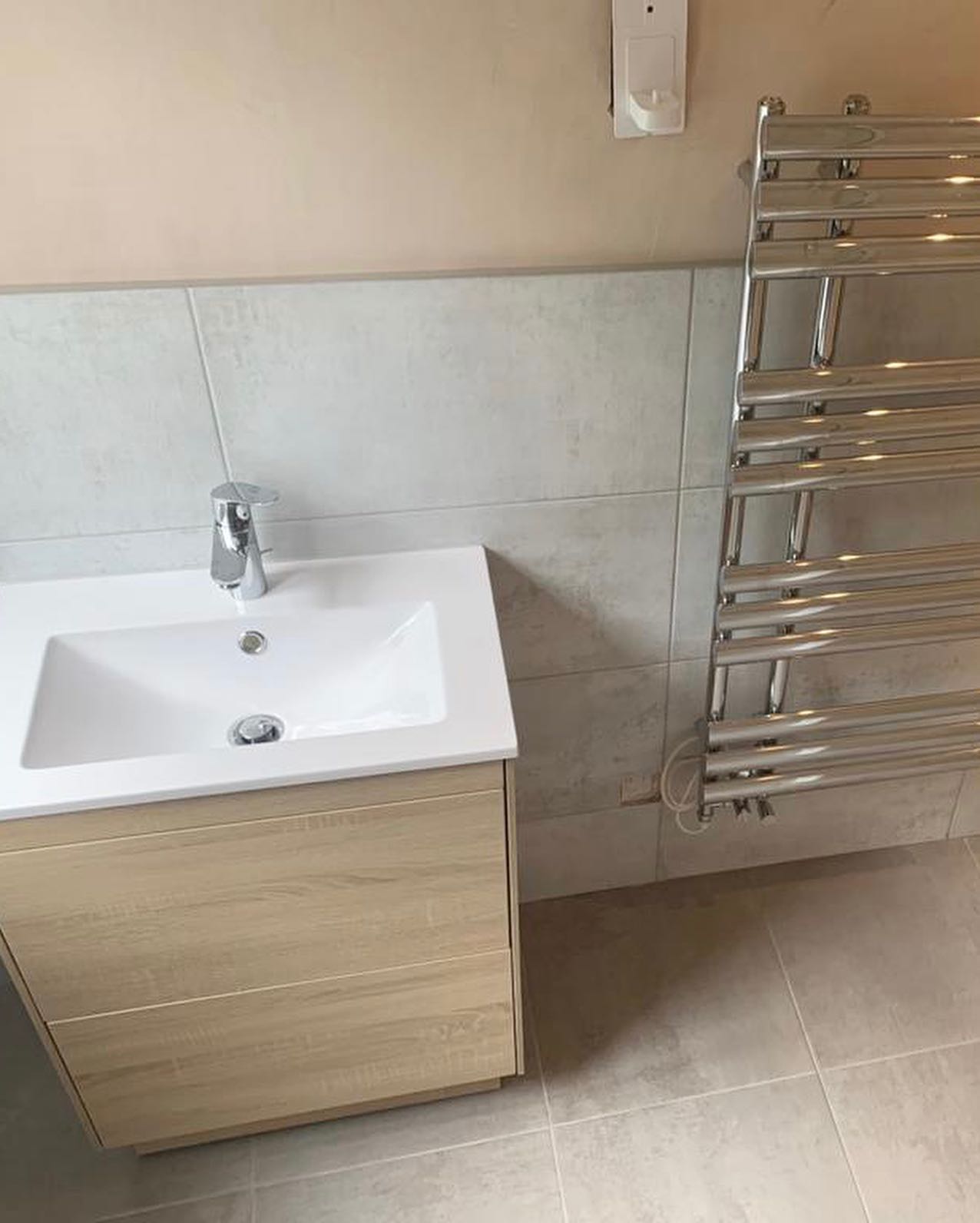Bathroom with a light wooden vanity, white sink, chrome faucet, towel rack, and tiled walls and floor.