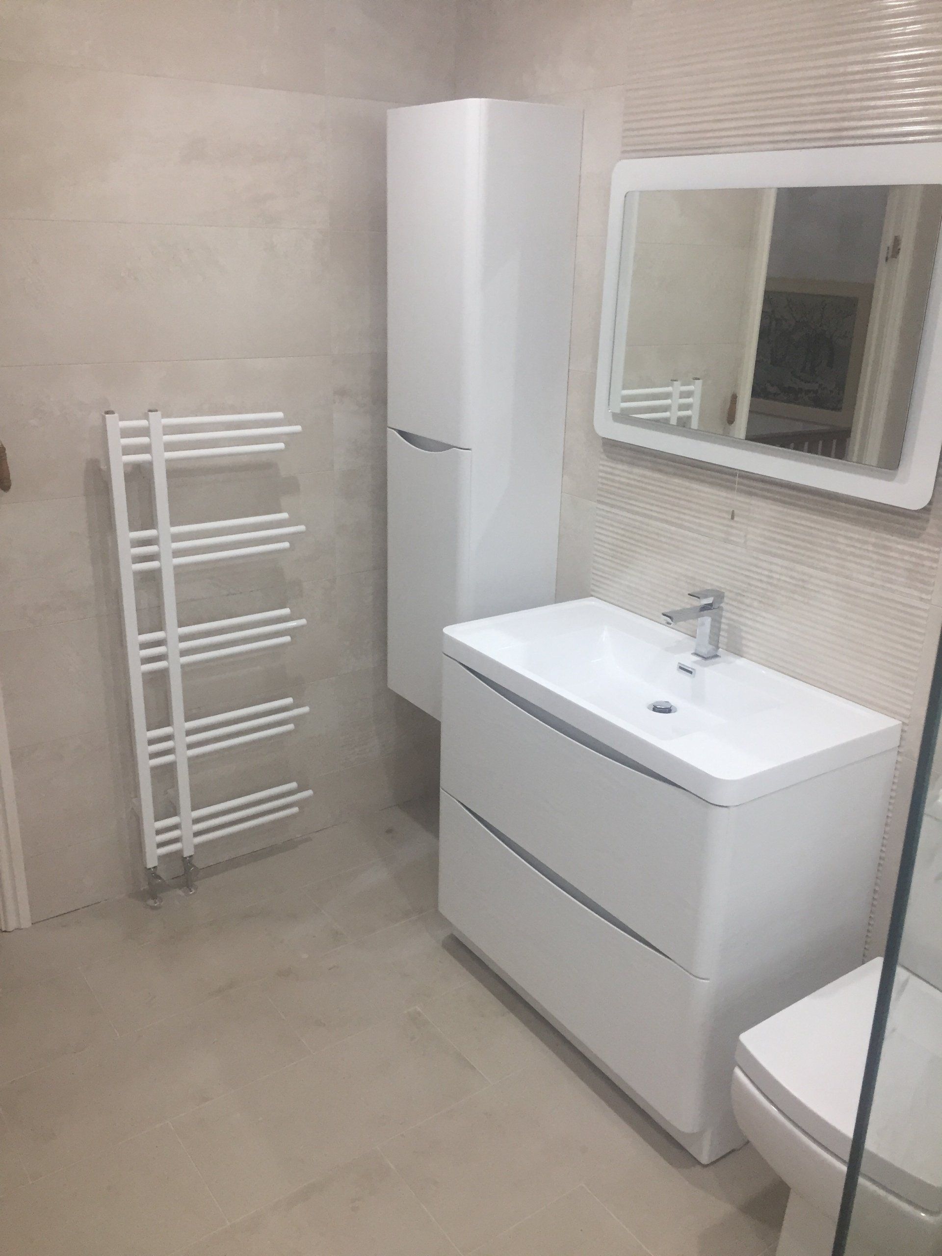 White modern bathroom with a sink, mirror, tall cabinet, towel rack, and toilet.