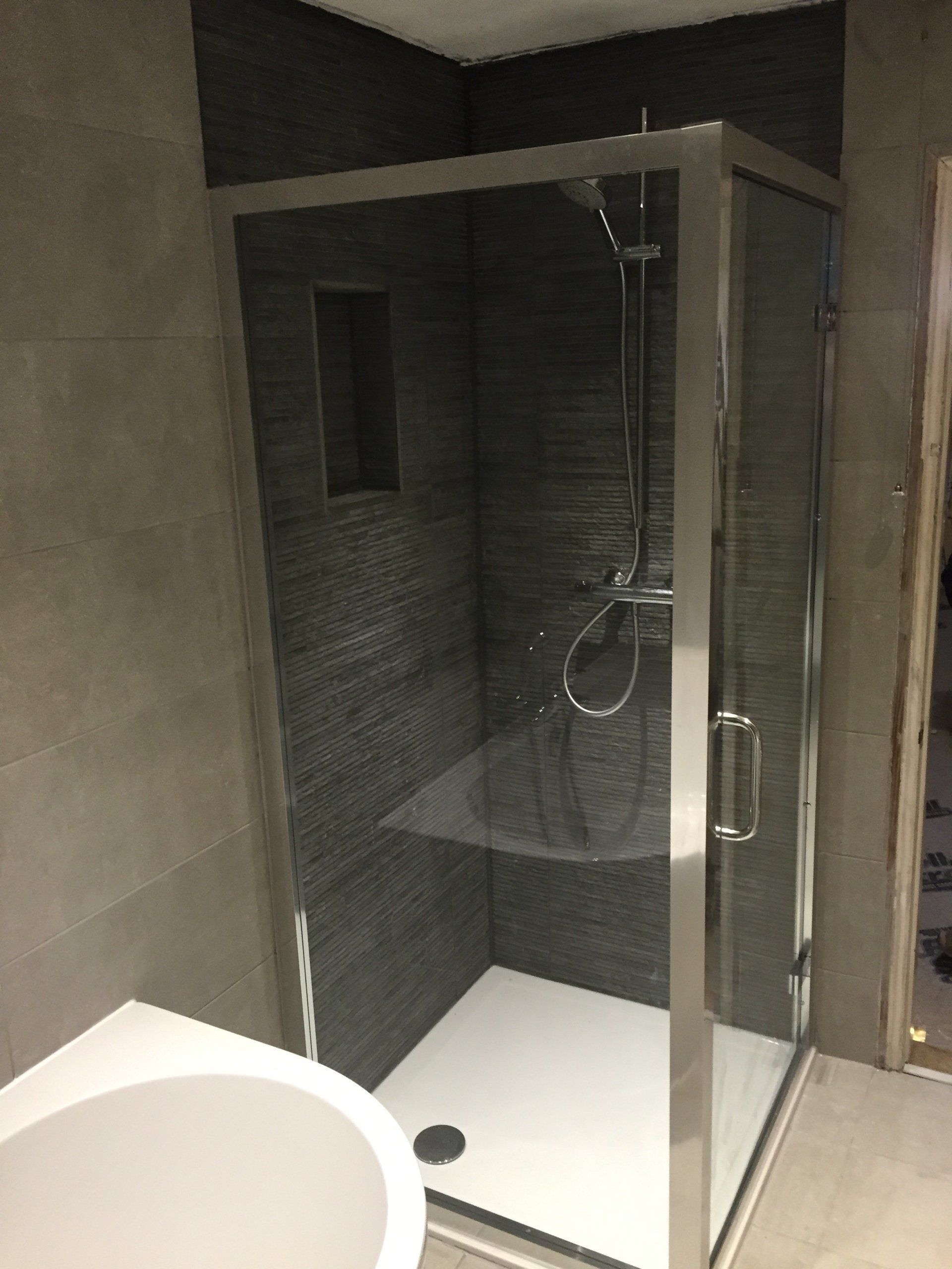 Shower stall with clear glass doors and a white base, gray tiled walls.