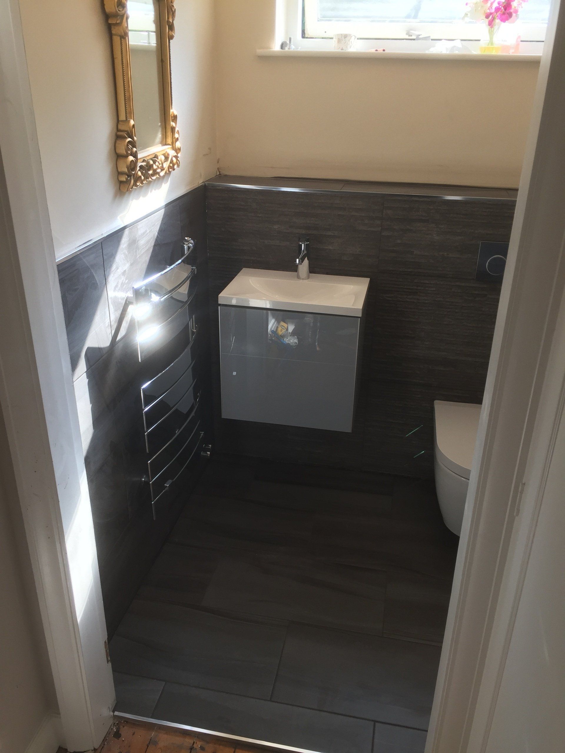 Small modern bathroom with gray wall-mounted sink, toilet, and dark wood-look tile.