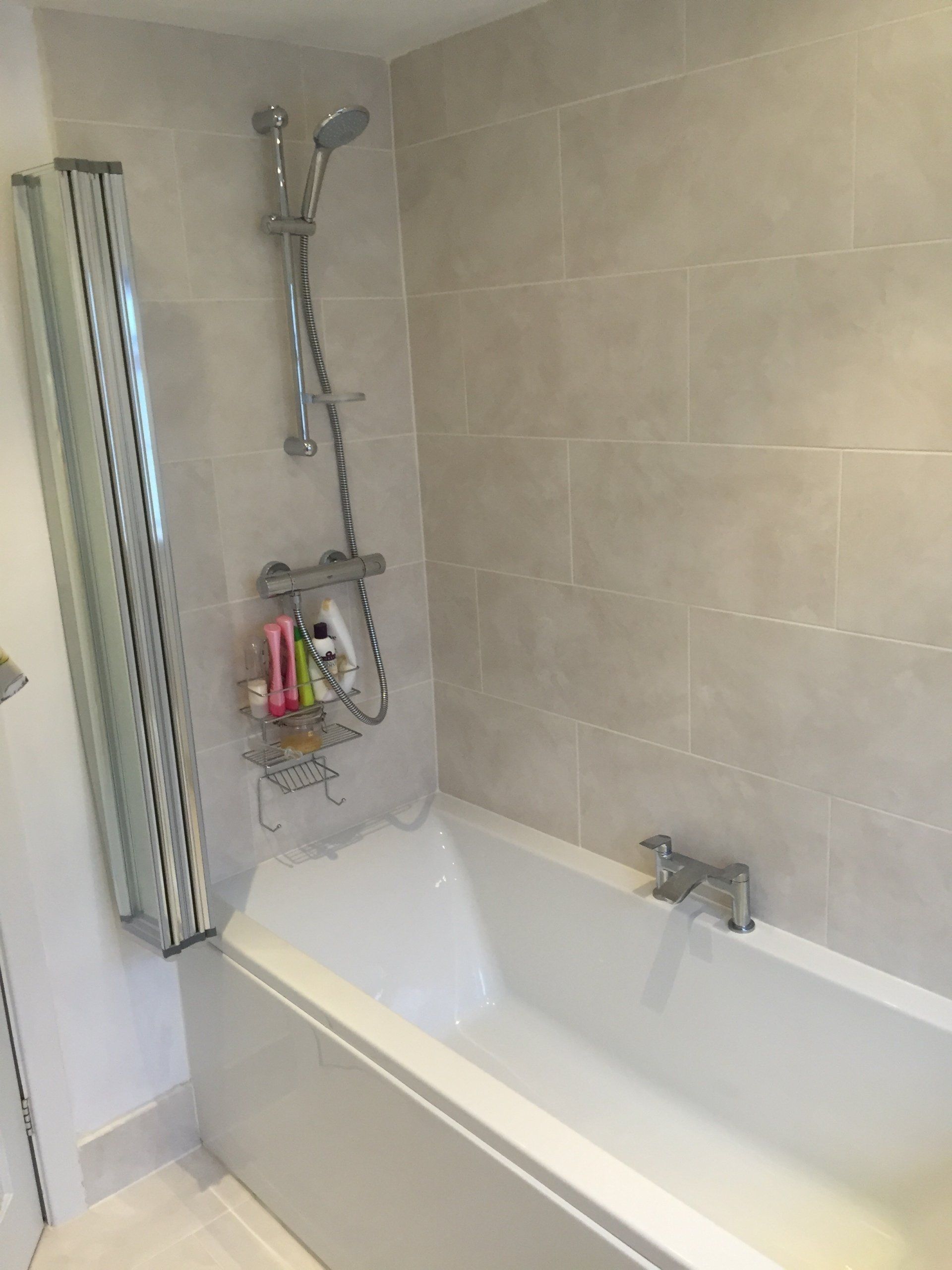 Bathroom with a white bathtub, showerhead, and light gray tiled walls.