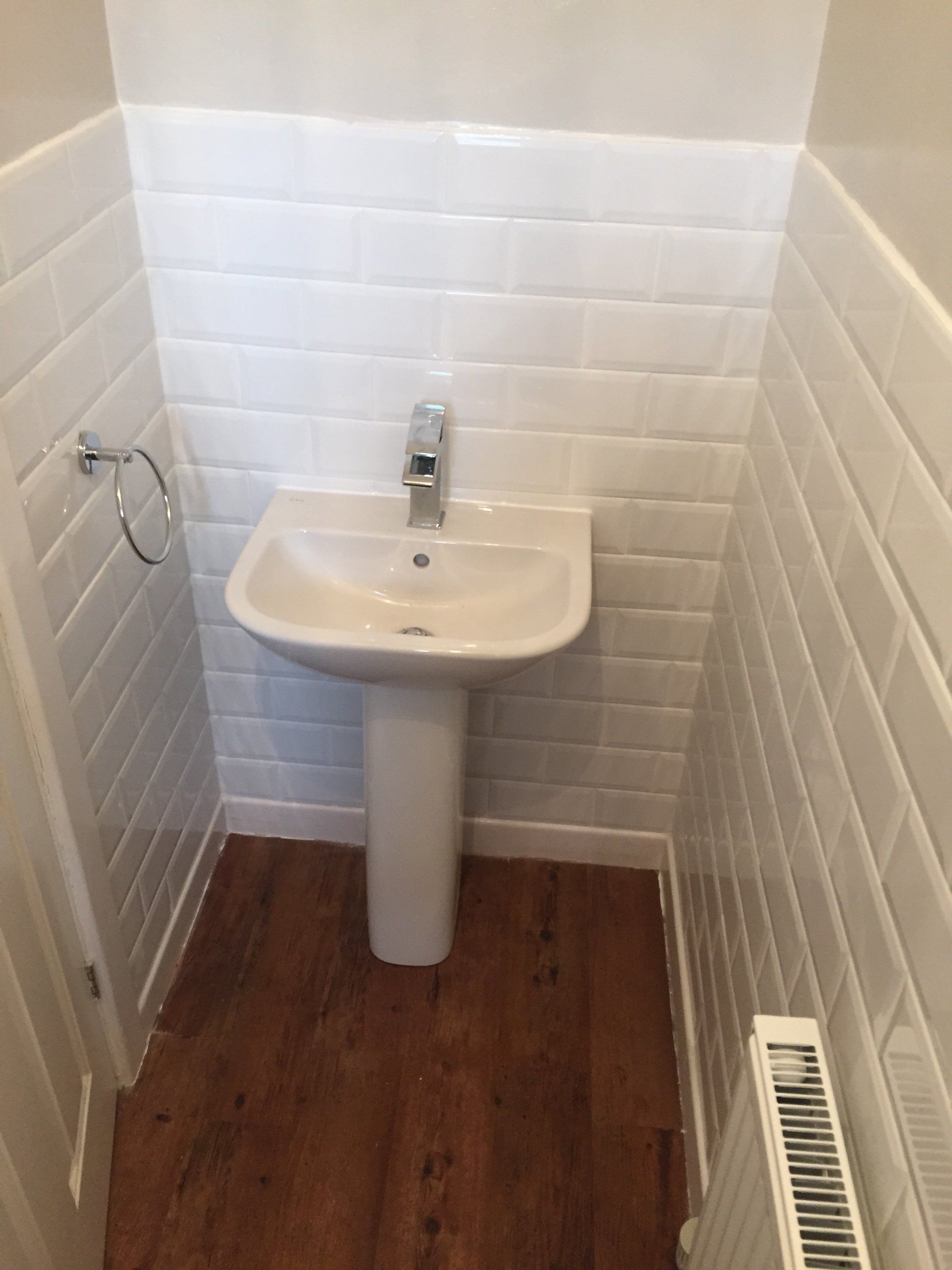 Small bathroom with pedestal sink and white tiled walls. Brown wooden floor and radiator.