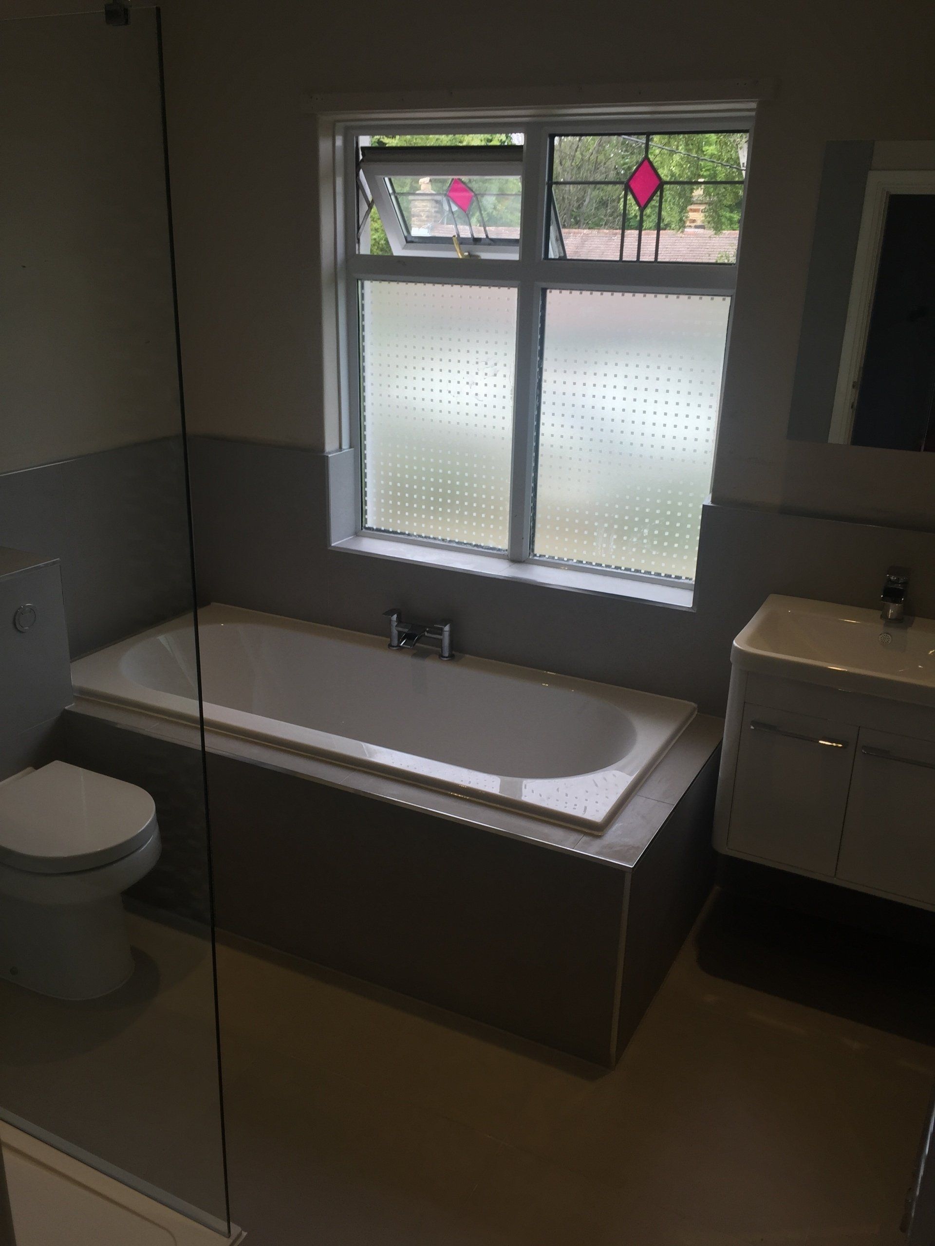 Bathroom with tub, toilet, and vanity. Frosted window above the tub, gray and white tones.