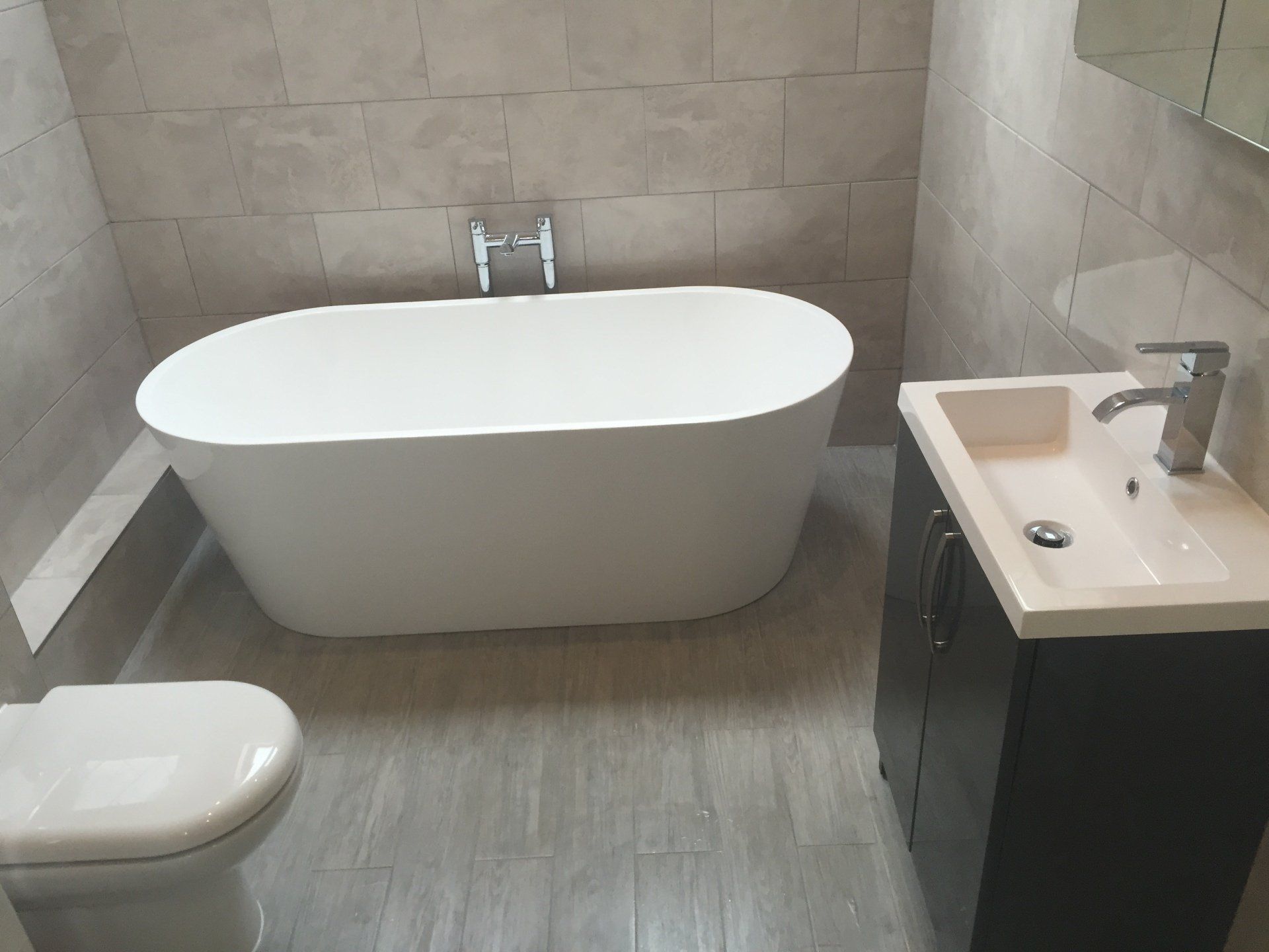 Bathroom with oval soaking tub, dark vanity, and toilet; light-colored tiles on the walls and floor.