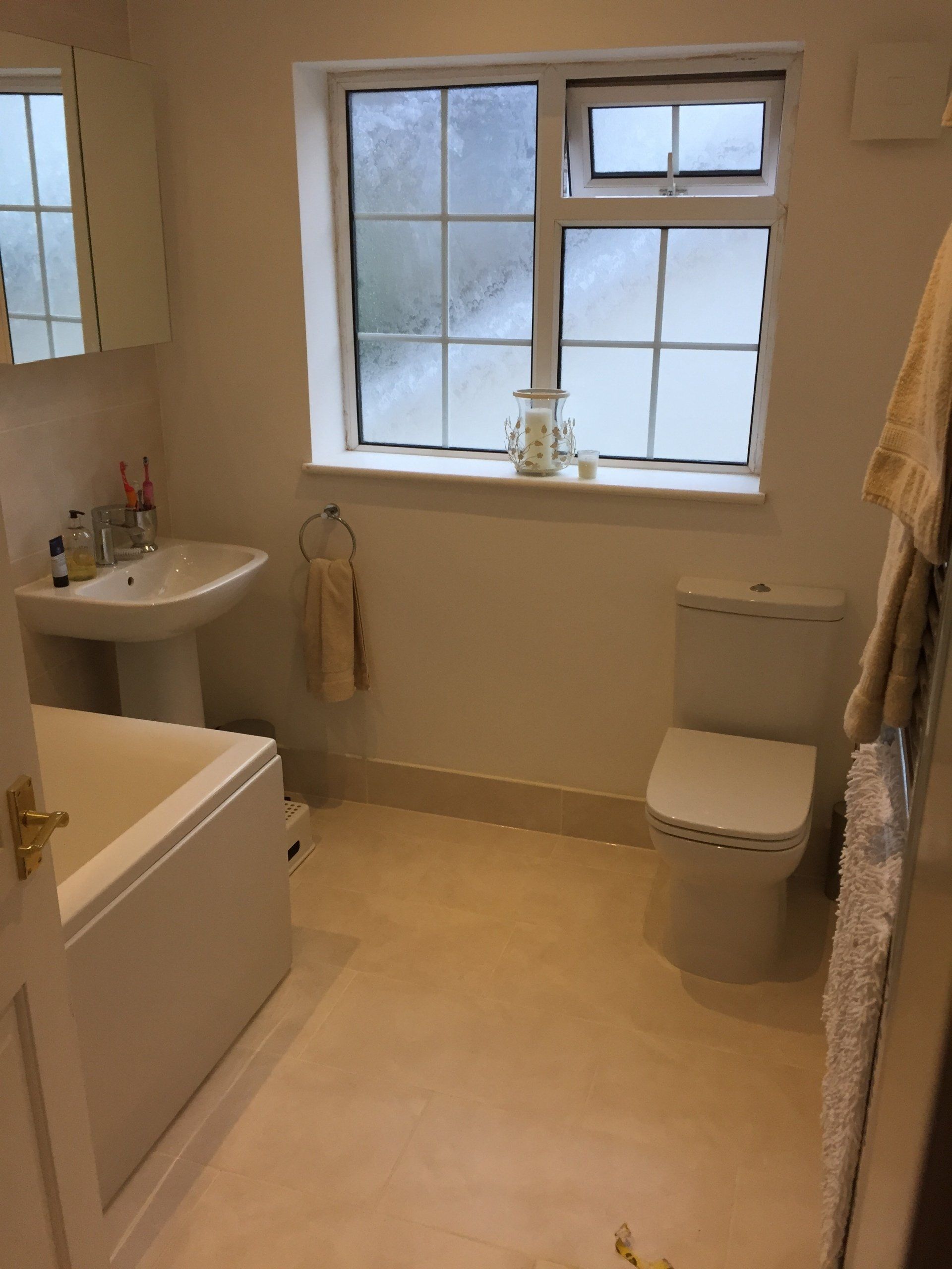 Bathroom with toilet, sink, tub, window, and neutral-colored walls and floor. A towel hangs near the window.