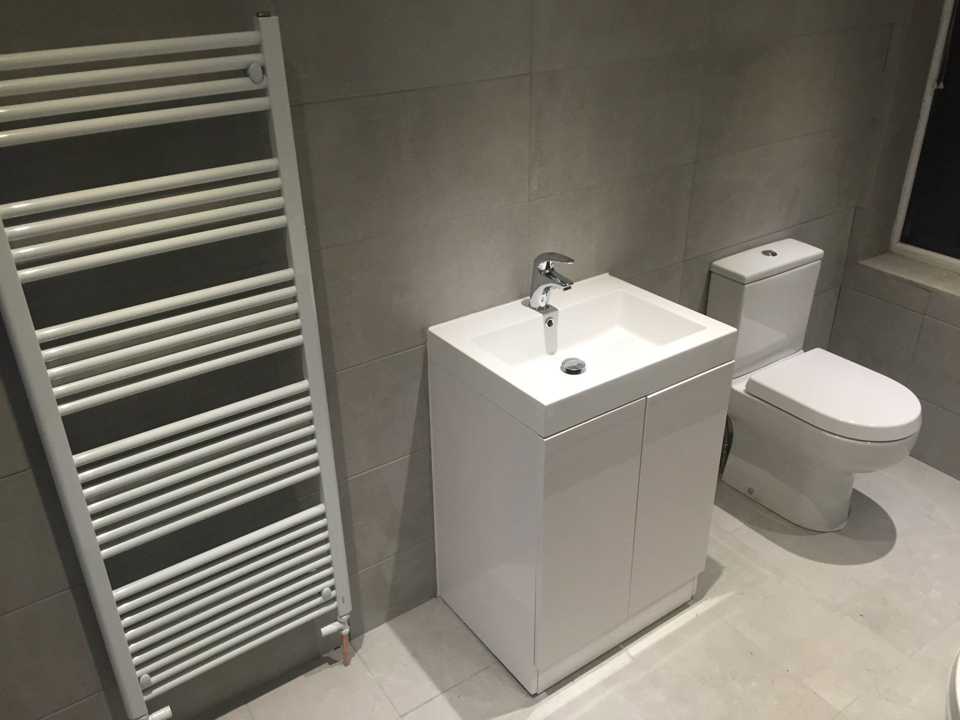 White bathroom with a heated towel rack, sink, and toilet.