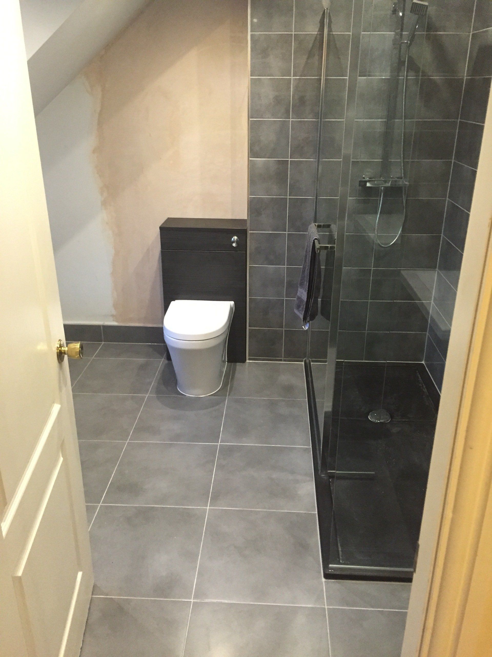 Bathroom with dark gray tiles, a toilet, and a glass shower.