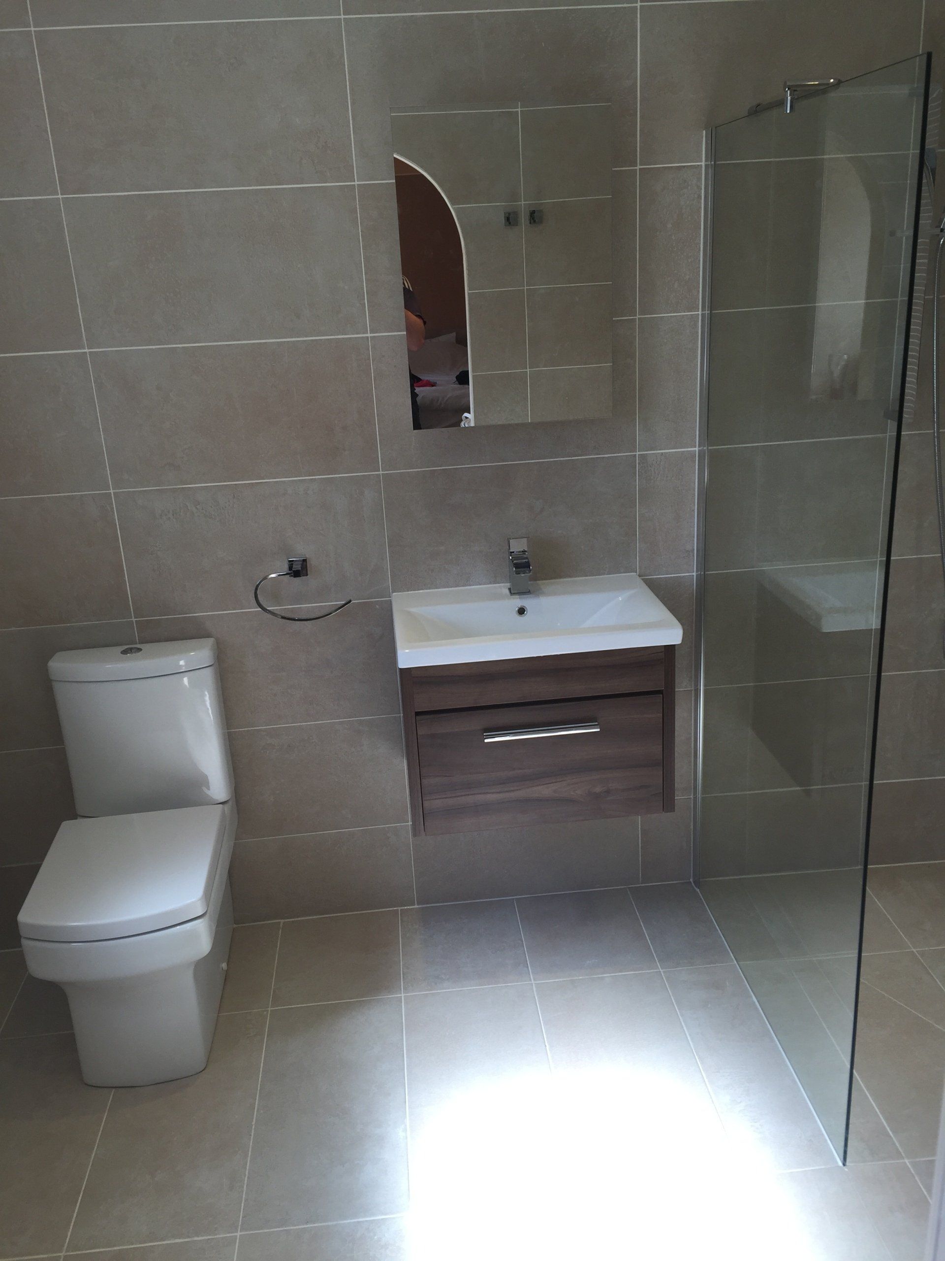 Bathroom with beige tile, toilet, sink with cabinet, mirror, and glass shower screen.