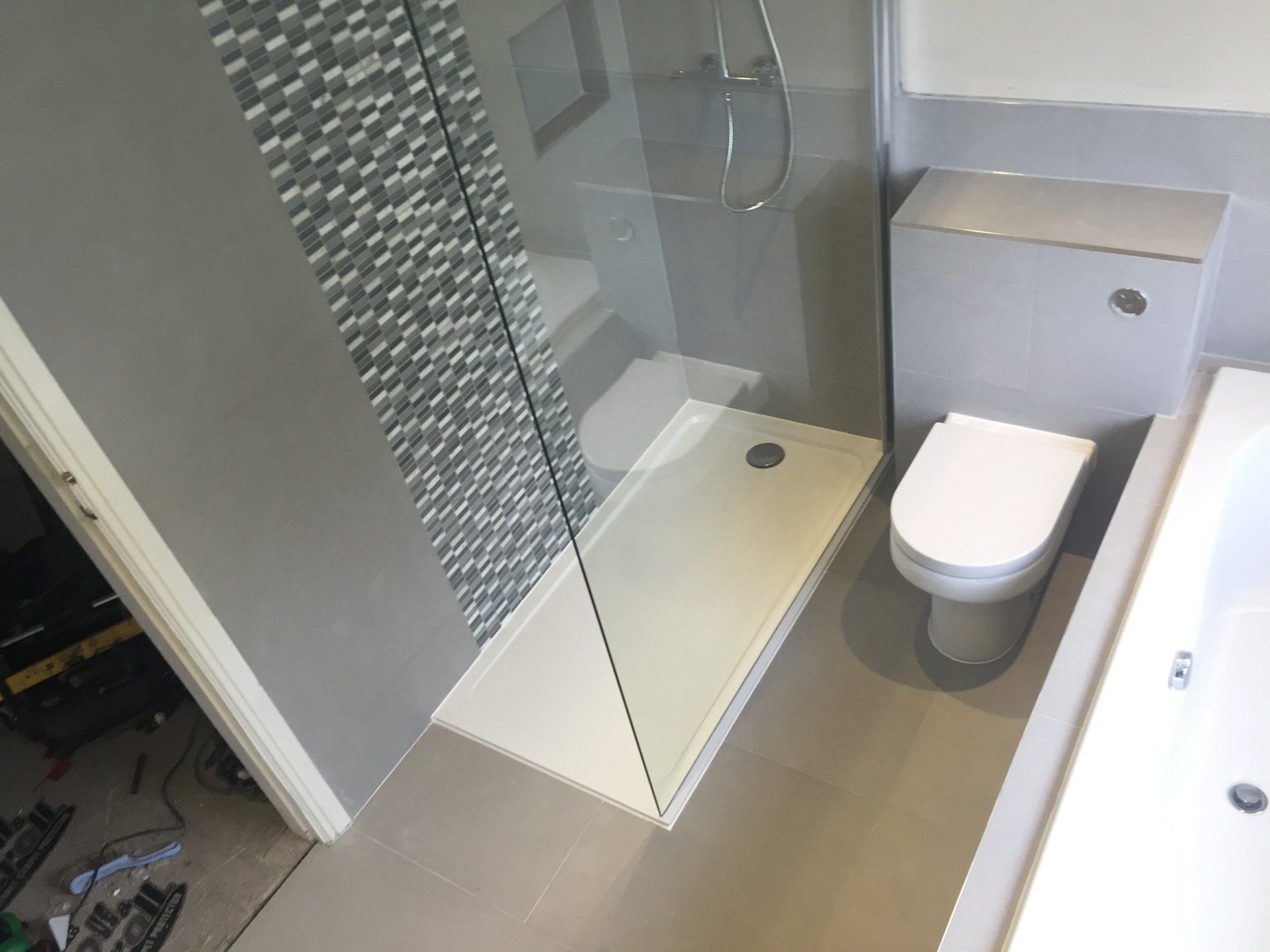 Modern bathroom with a glass shower, toilet, and gray tiled walls.