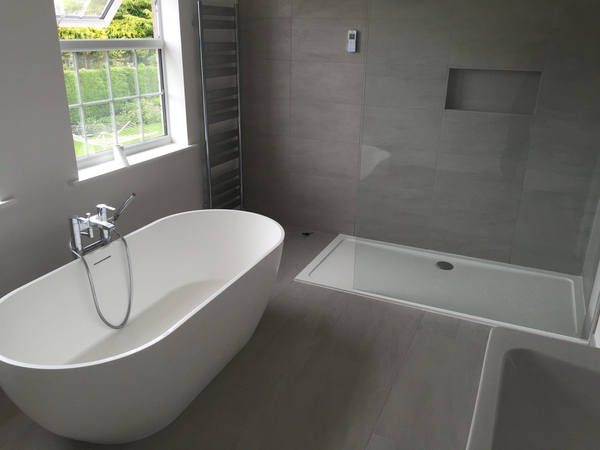 Modern bathroom with freestanding tub, shower, heated towel rack, and large window. Grey tile walls.