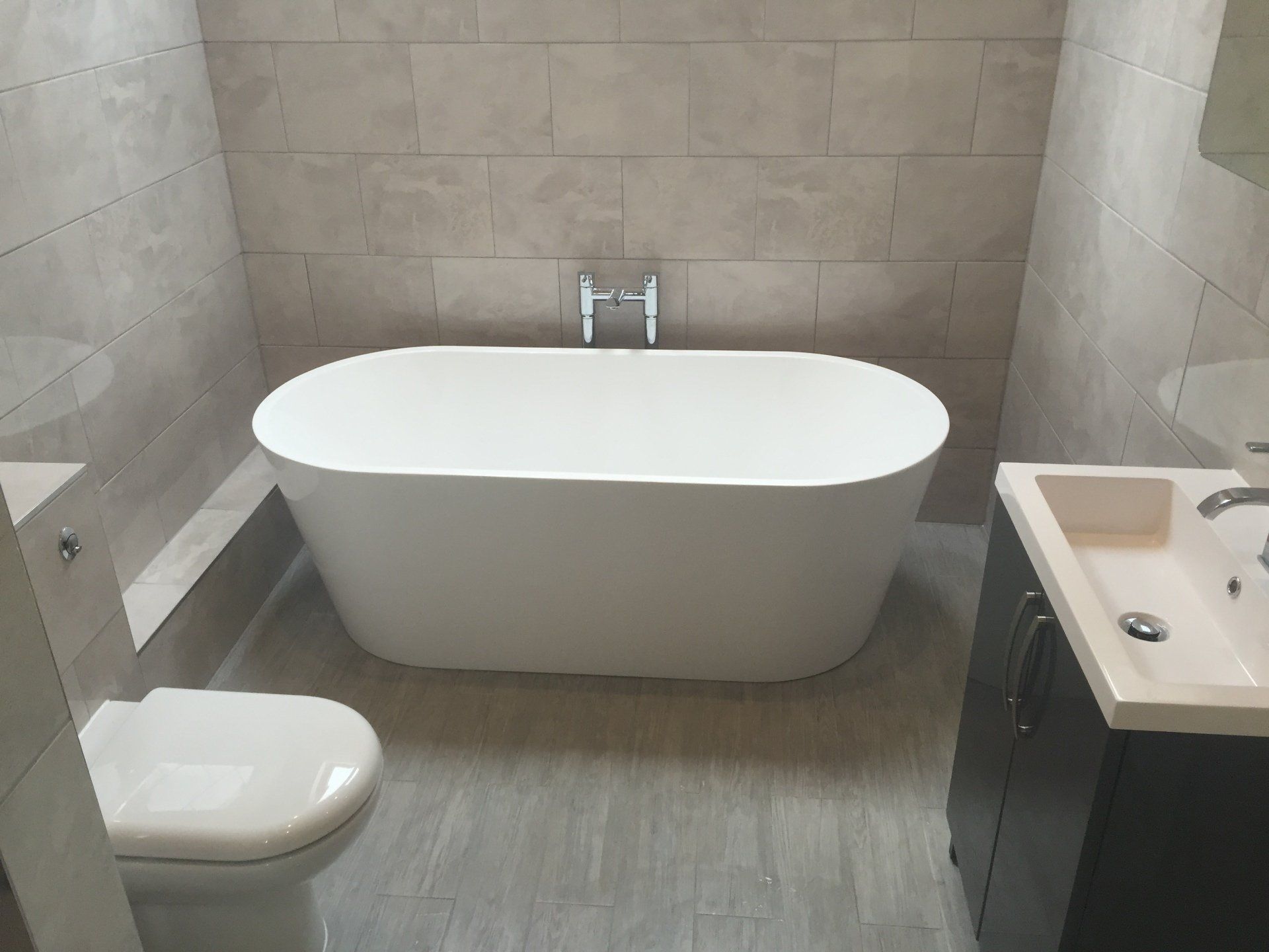Bathroom with a white oval bathtub, beige tile walls, and a toilet and sink.