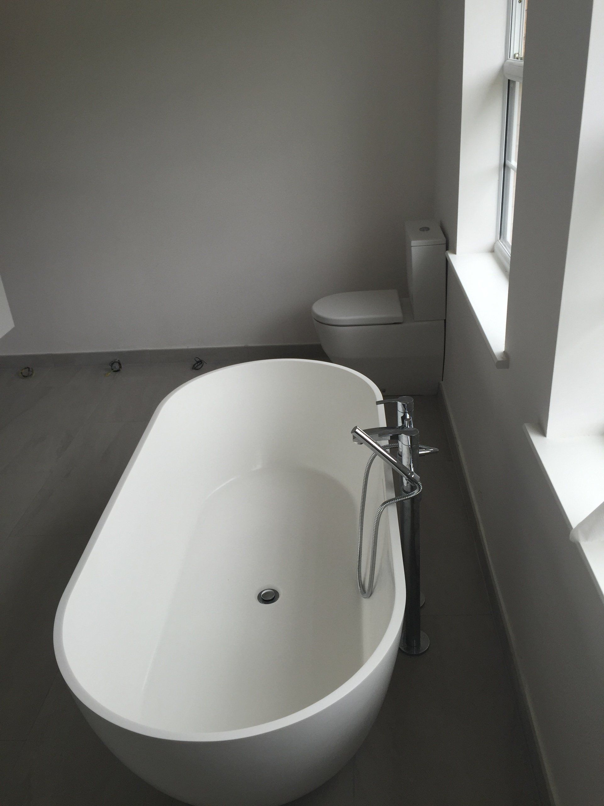 White bathtub and toilet in a modern bathroom with window on the right.