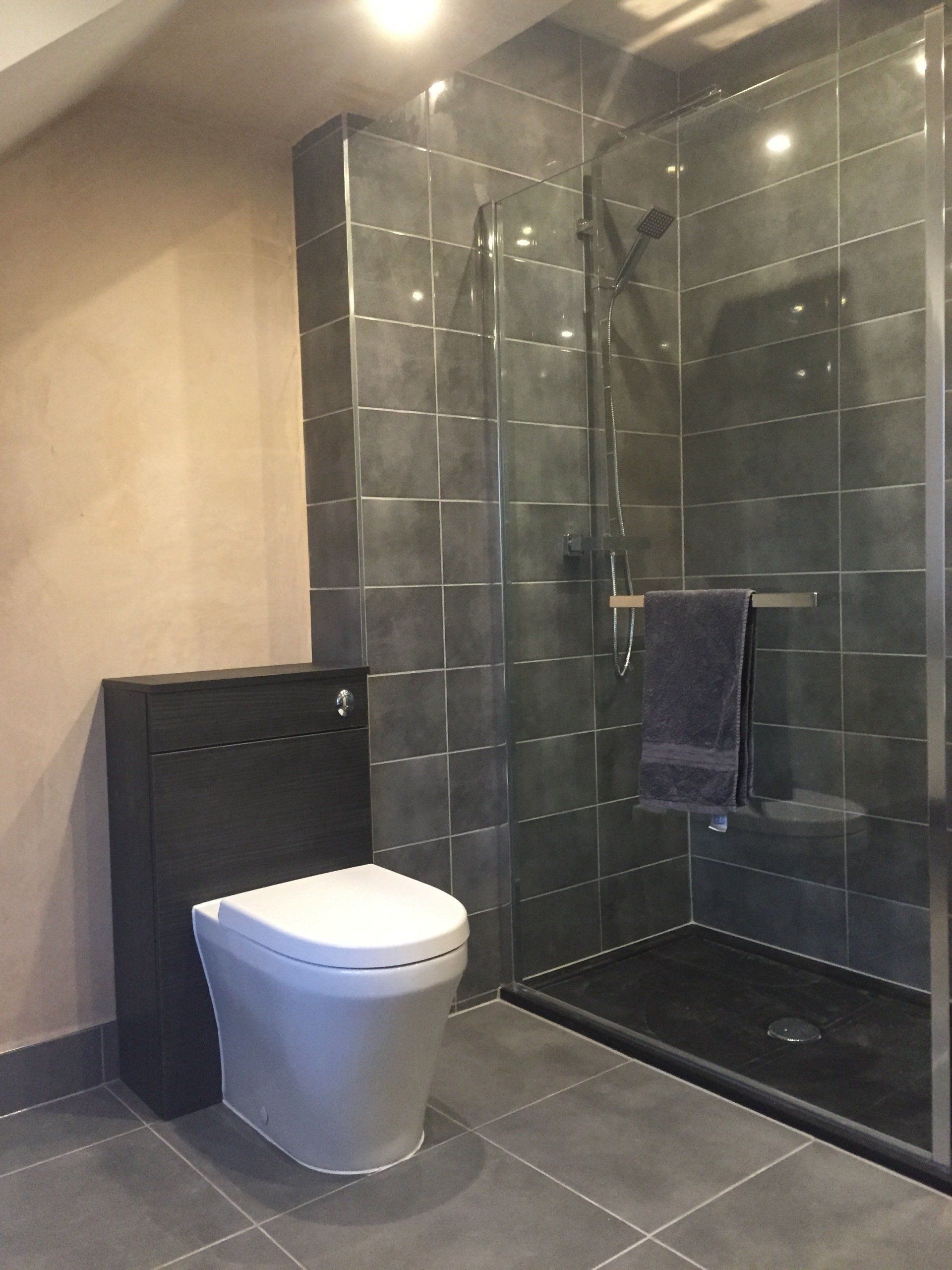 Bathroom with gray tile shower, black toilet, and towel.