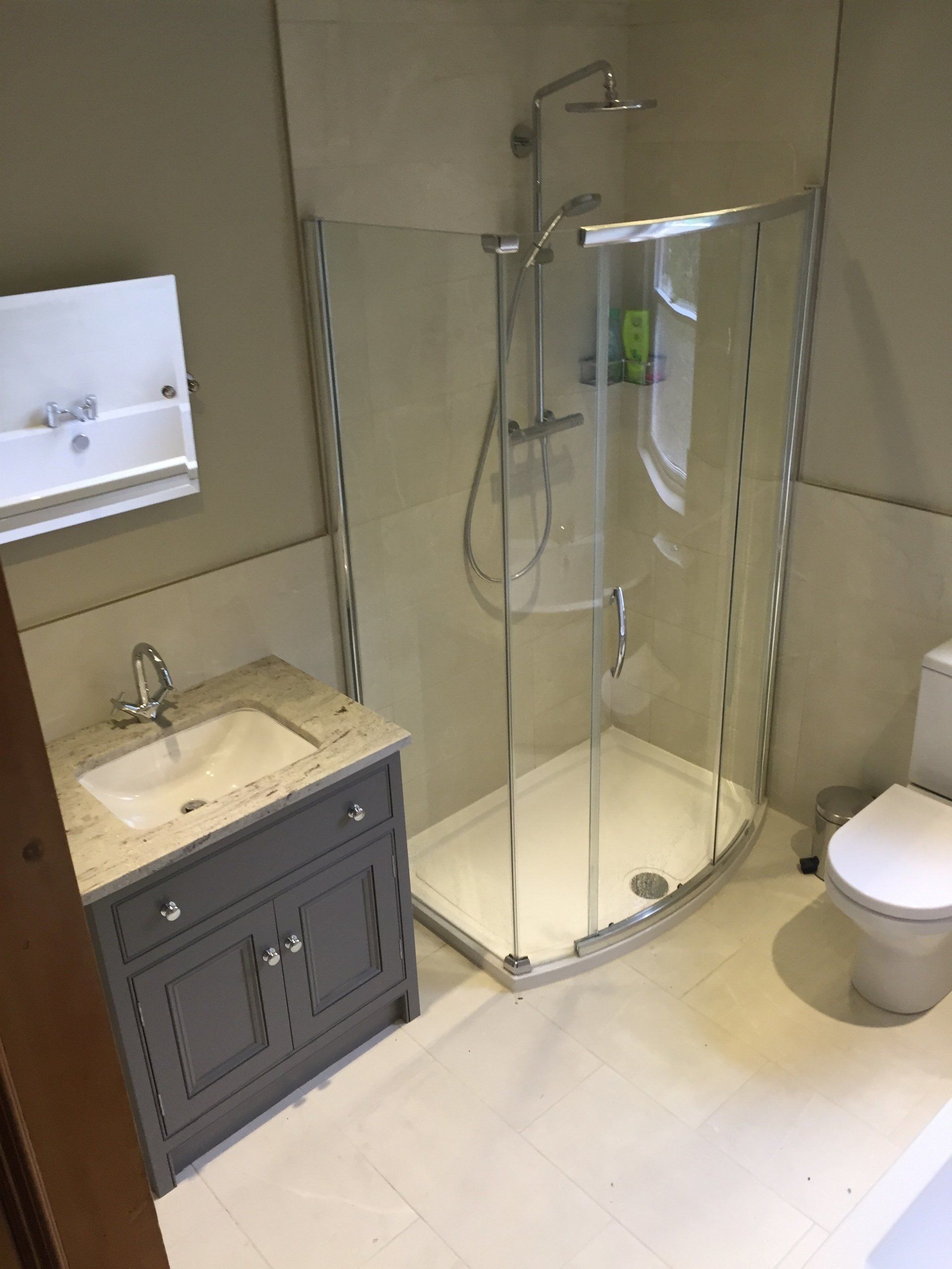 Bathroom with gray vanity, curved glass shower, and white toilet.