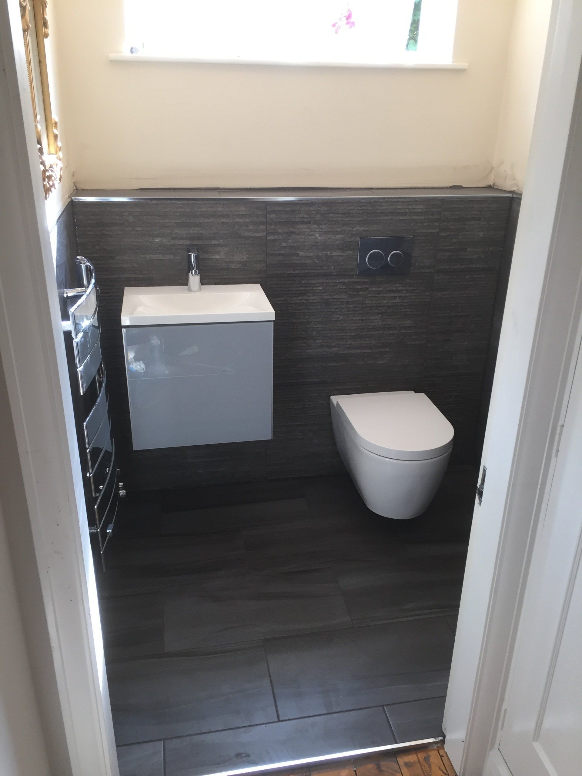 Modern bathroom with gray tiles, floating sink, toilet, and window.