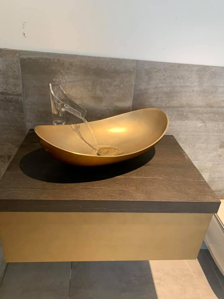 Gold vessel sink with flowing water, mounted on a dark wood cabinet.