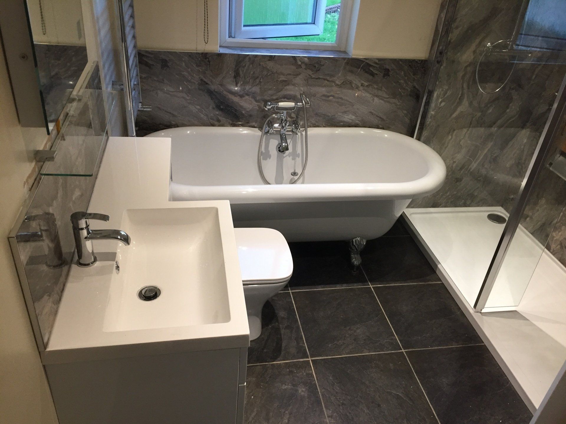 Modern bathroom with white tub, sink, and toilet, dark gray tile, marble-look wall. Shower on the right.