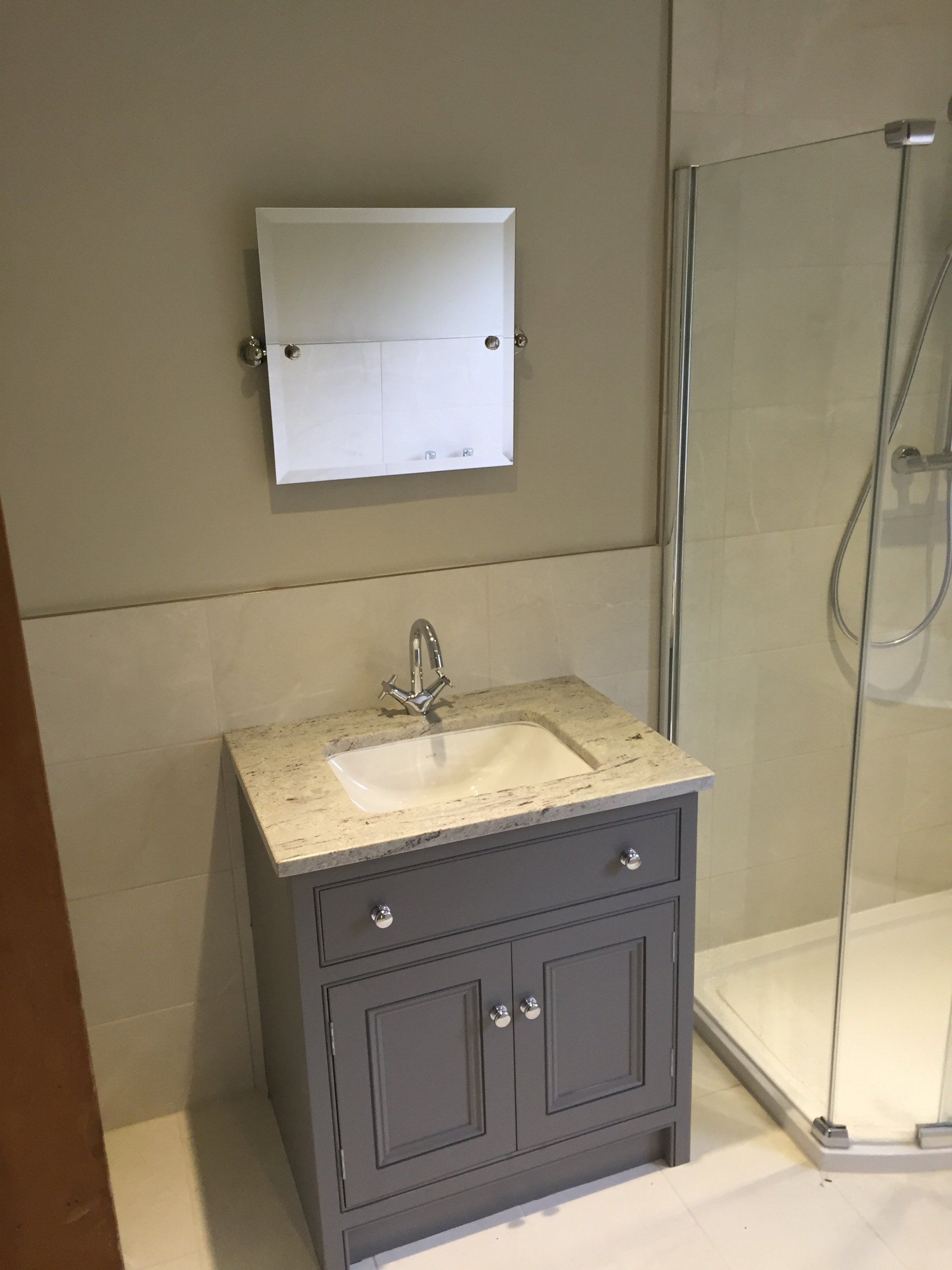 Gray bathroom vanity with a white sink, mirror, and shower.