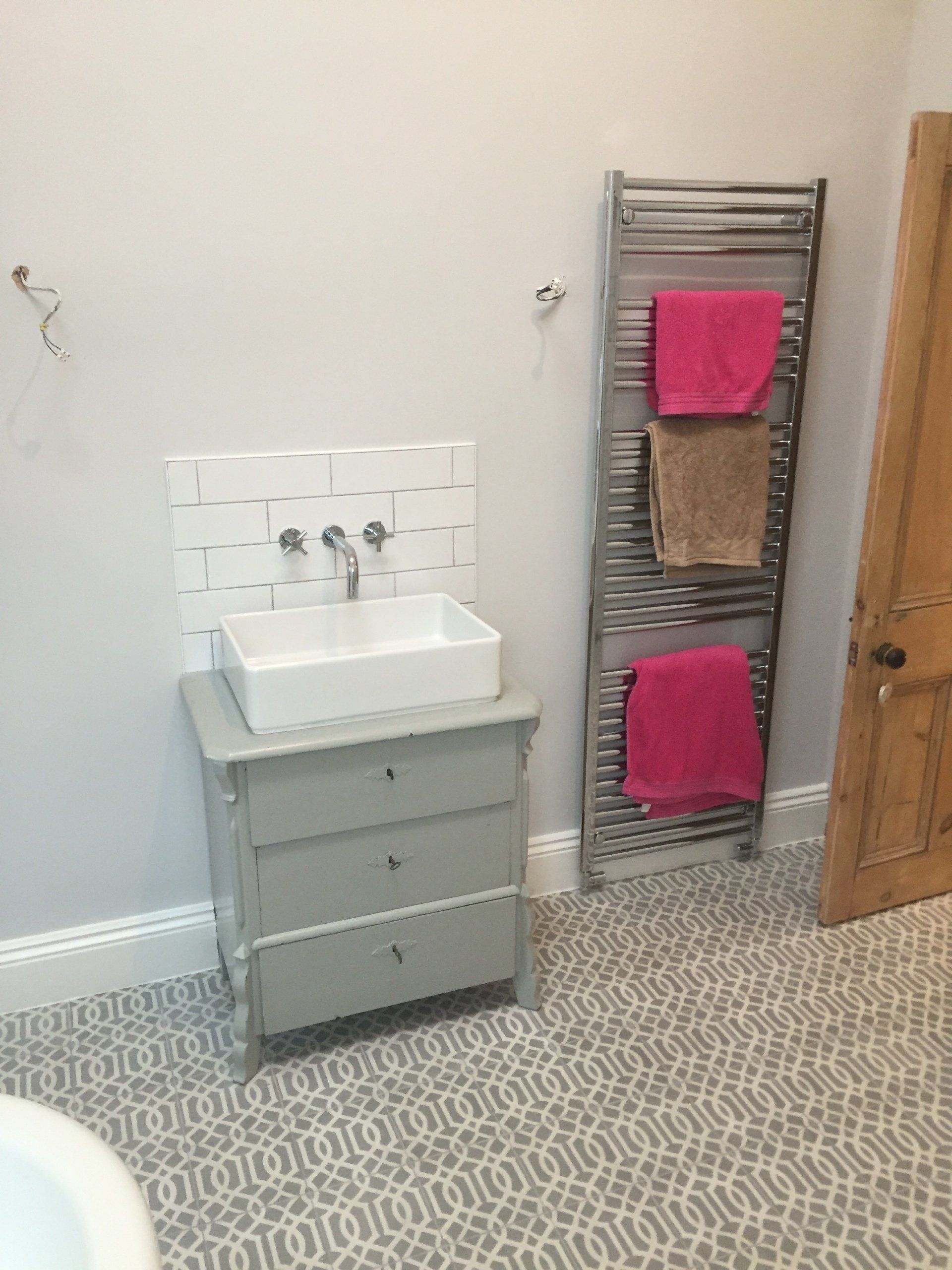 Bathroom with a gray vanity, white sink, and tiled backsplash. A towel rack with pink and brown towels is visible.