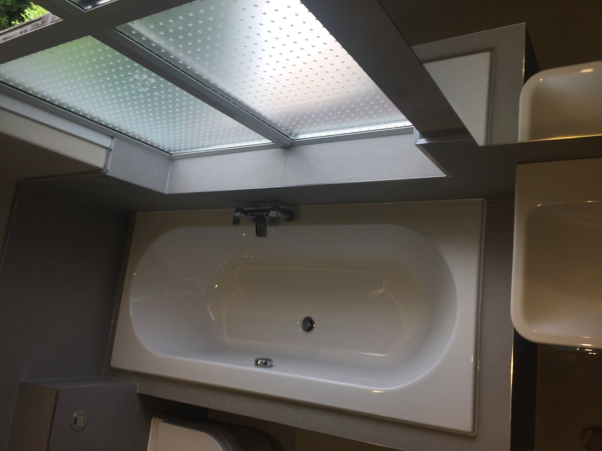 White bathtub under a frosted skylight in a bathroom setting.
