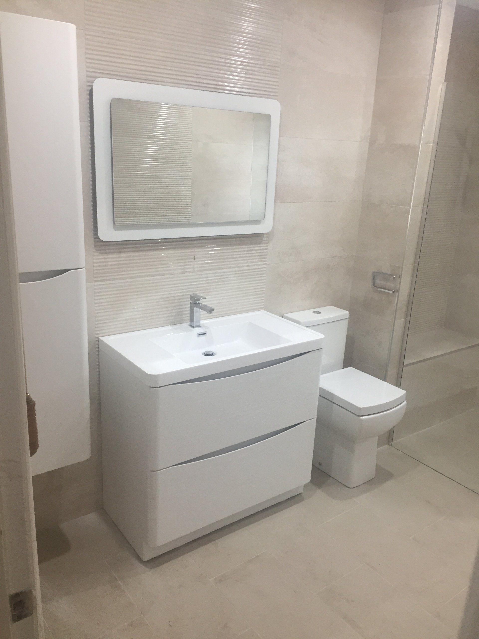 White bathroom with a vanity, toilet, mirror, and tall storage cabinet.