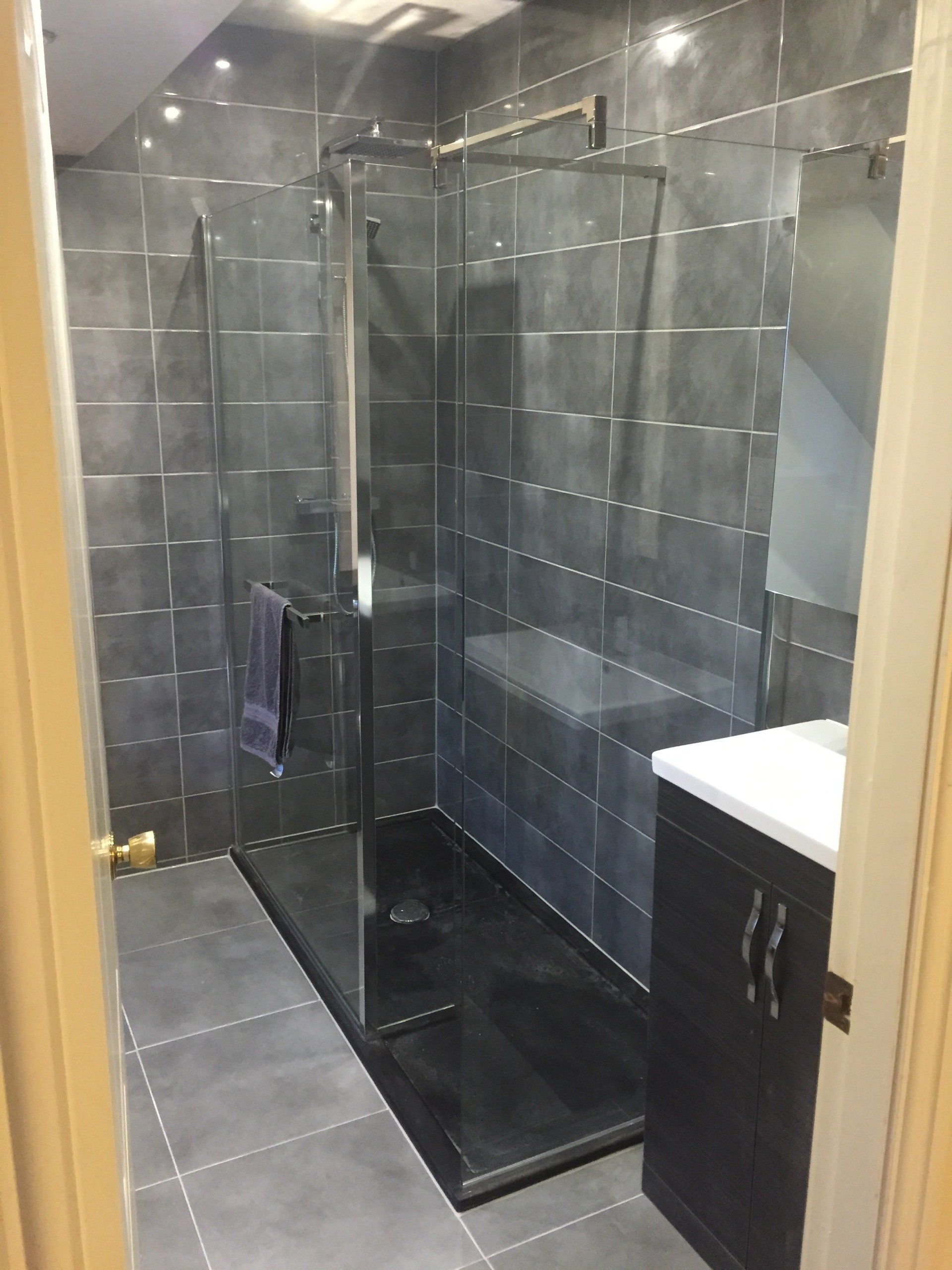 Modern bathroom with a glass-enclosed shower, dark gray tiles, and a dark cabinet with a white countertop.
