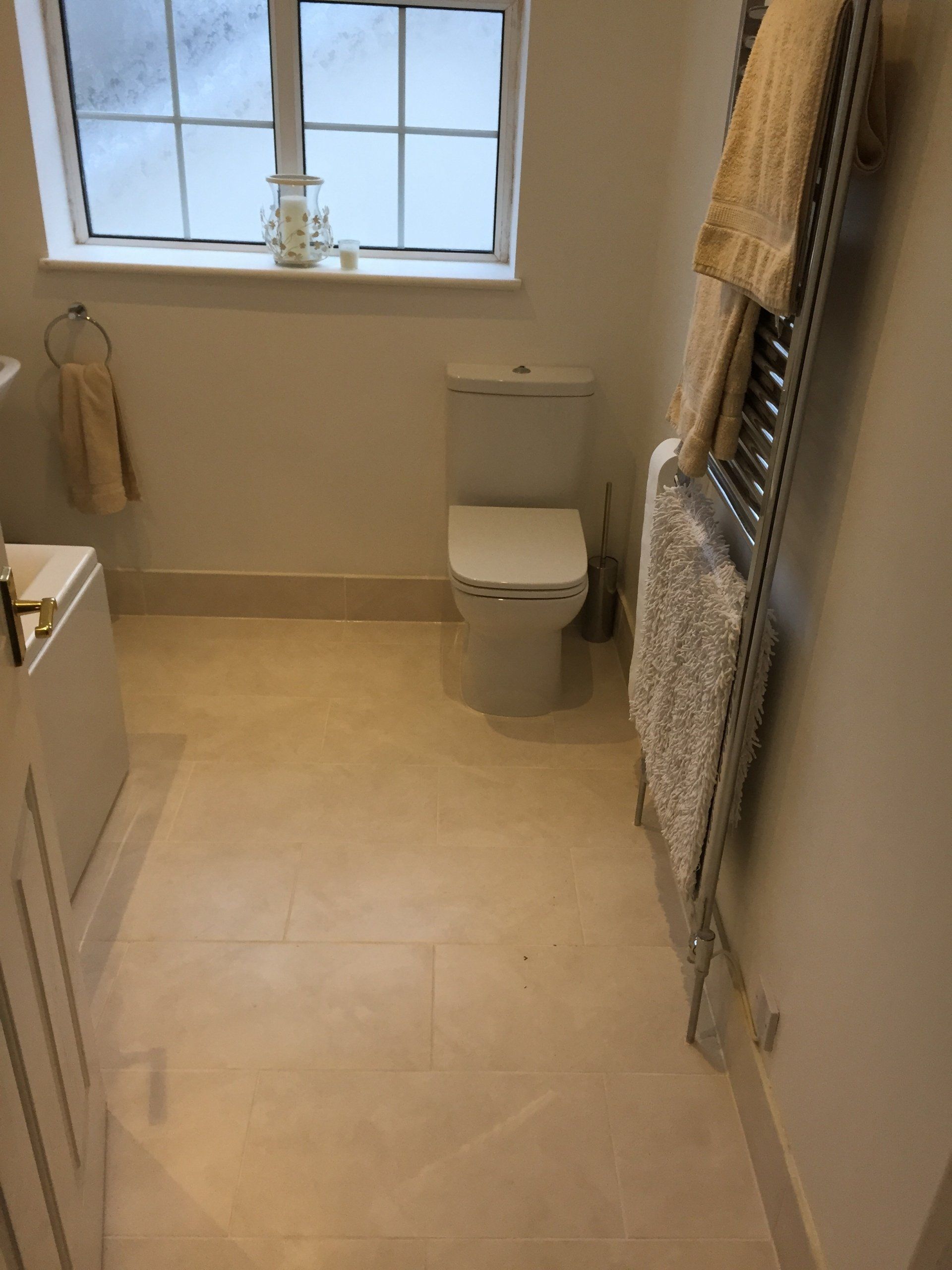 A small bathroom with a toilet, window, towel rack, and beige tile floor.