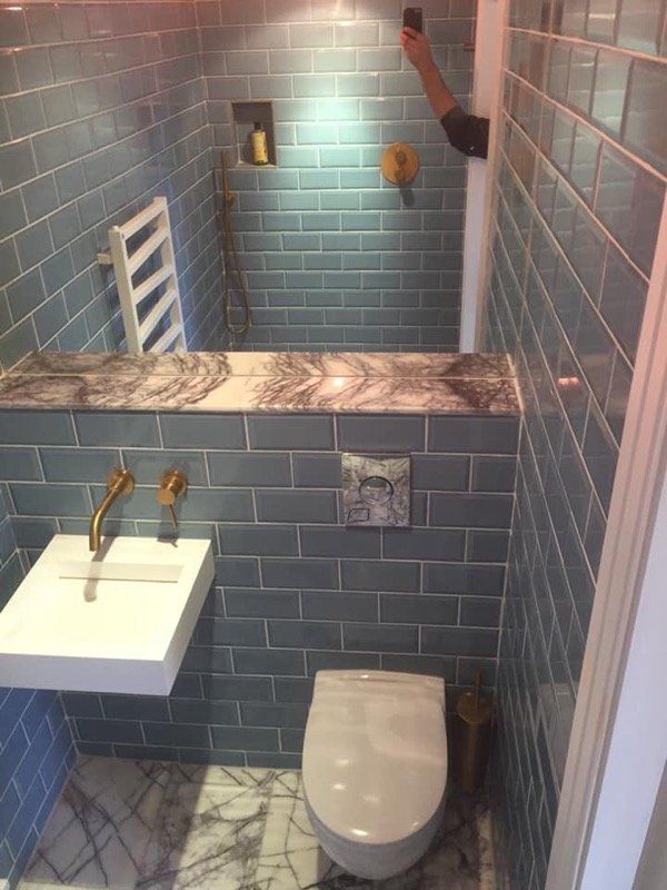 Small bathroom with blue tiled walls, white sink, and toilet, marble accent, gold fixtures.