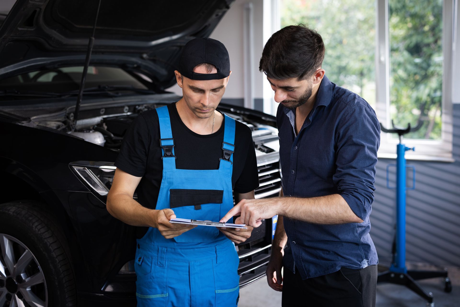 car service manager with a tablet talking to mechanic man discussing car diagnostics and repairing
