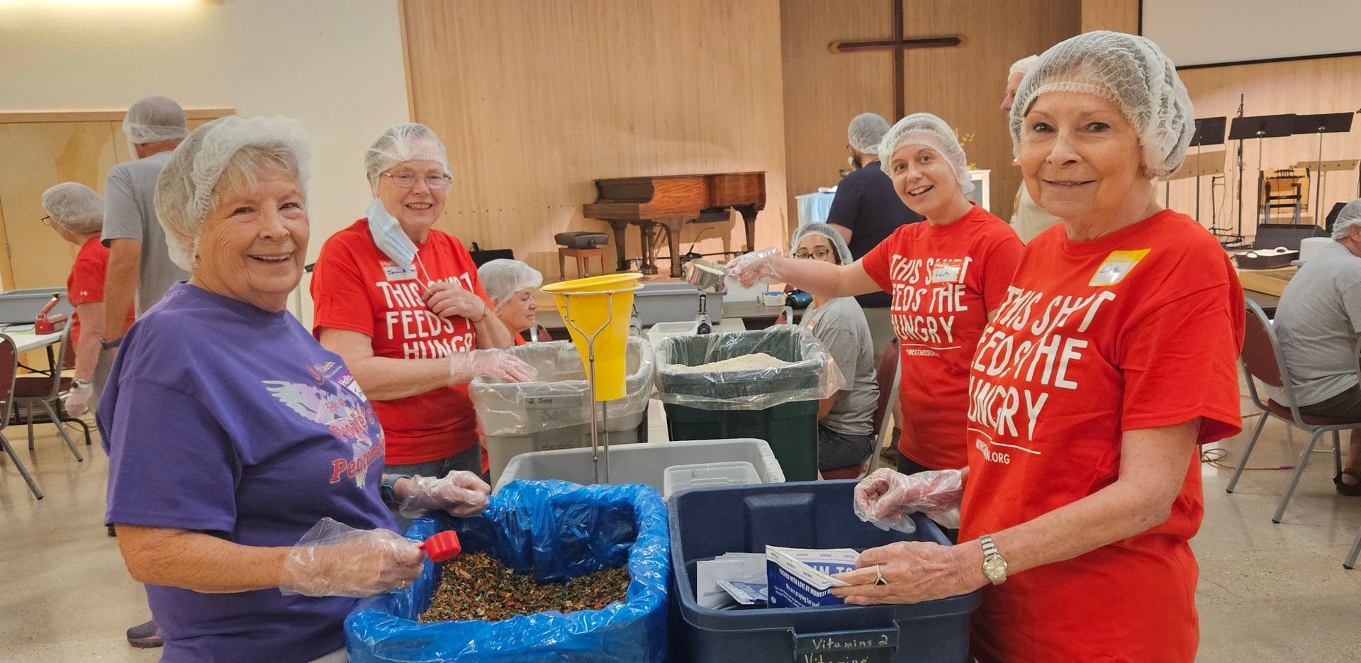 People packing food boxes for donation at tables indoors near a Christmas tree.