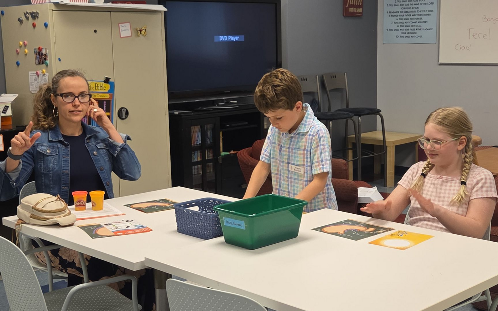 Man demonstrating to children at a table in a classroom, with small containers and supplies.