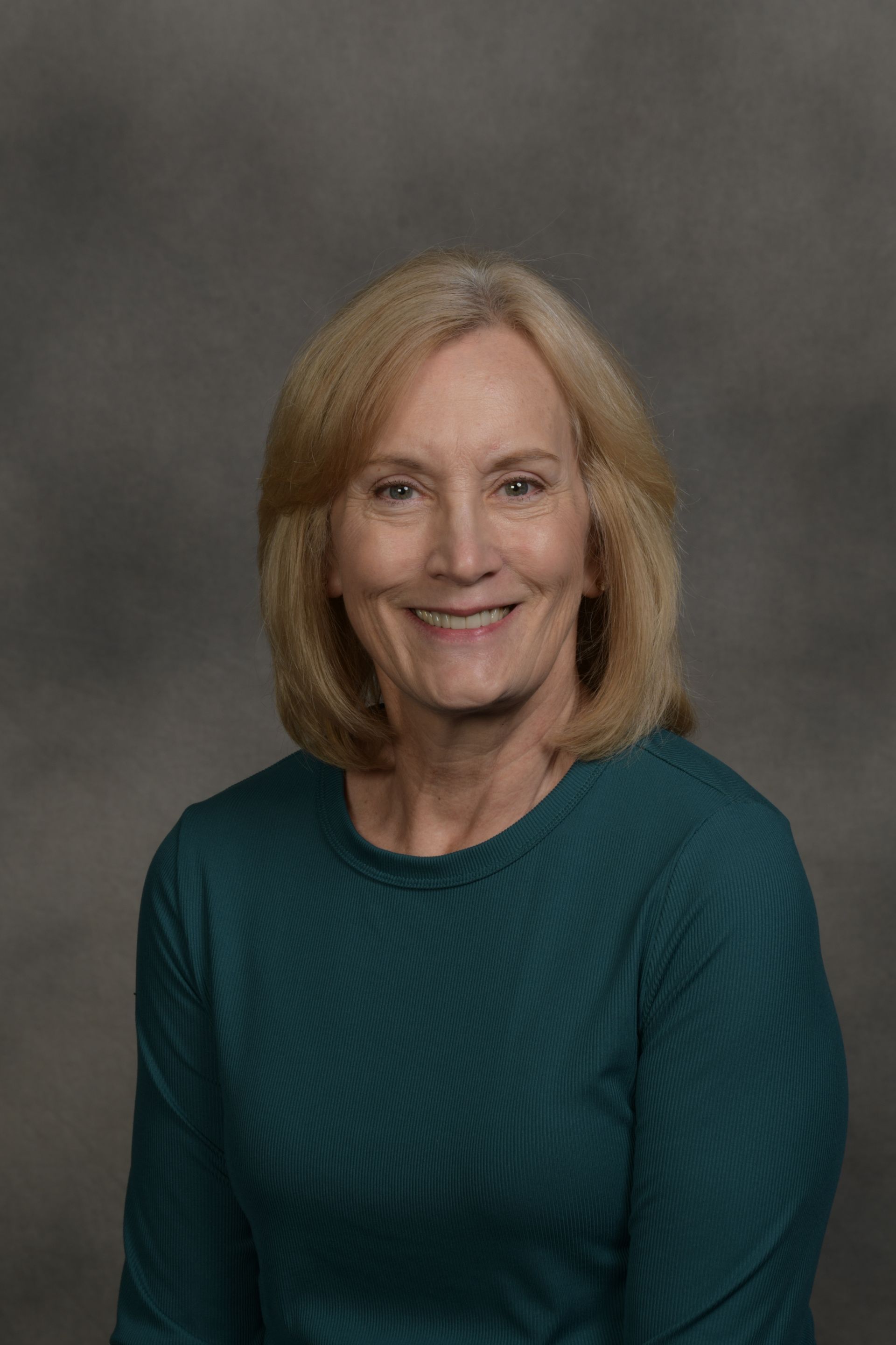 Woman wearing glasses smiles at the camera in front of a brick wall.