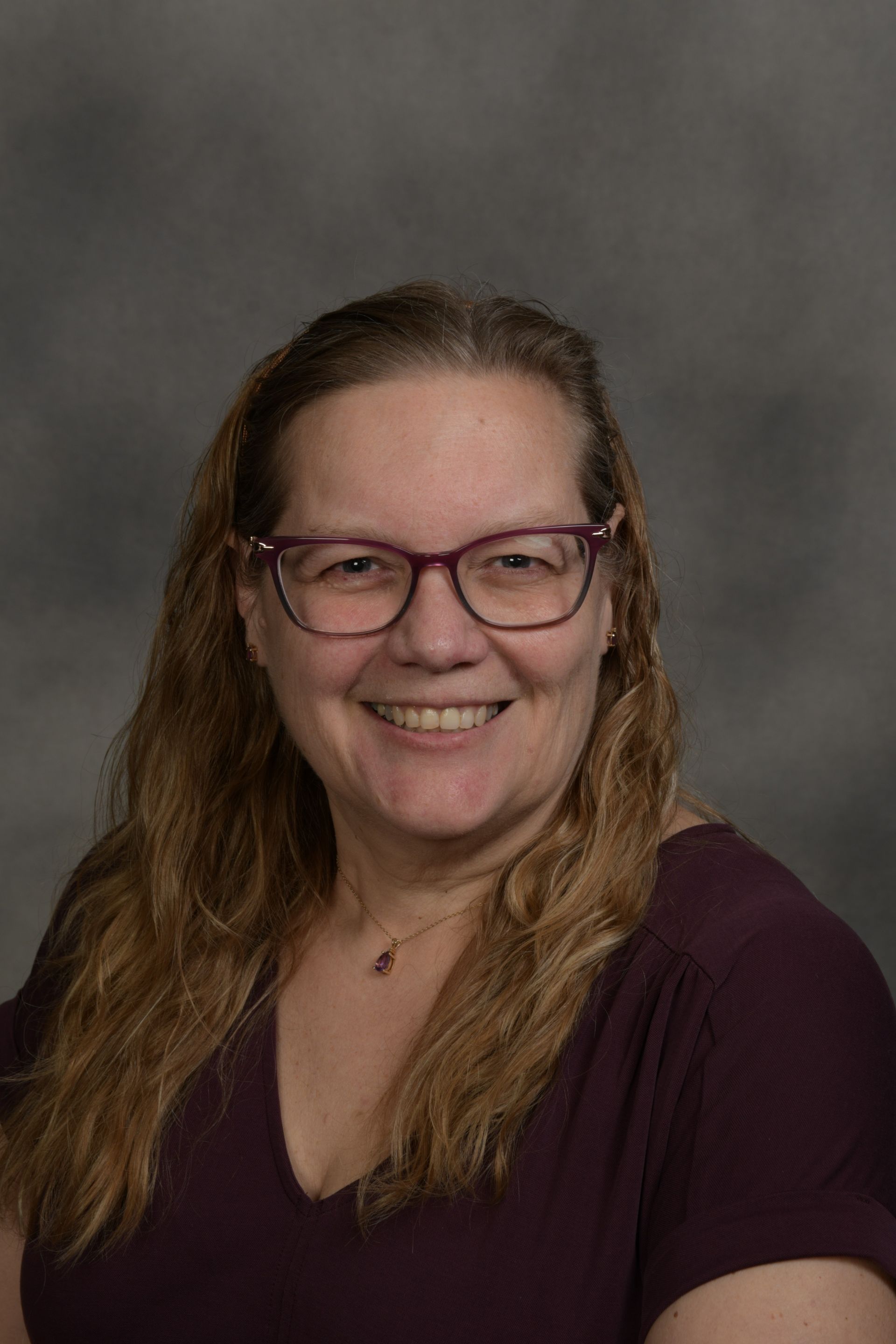 Woman wearing glasses smiles at the camera in front of a brick wall.