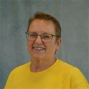 A woman wearing glasses and a yellow shirt is smiling for the camera.