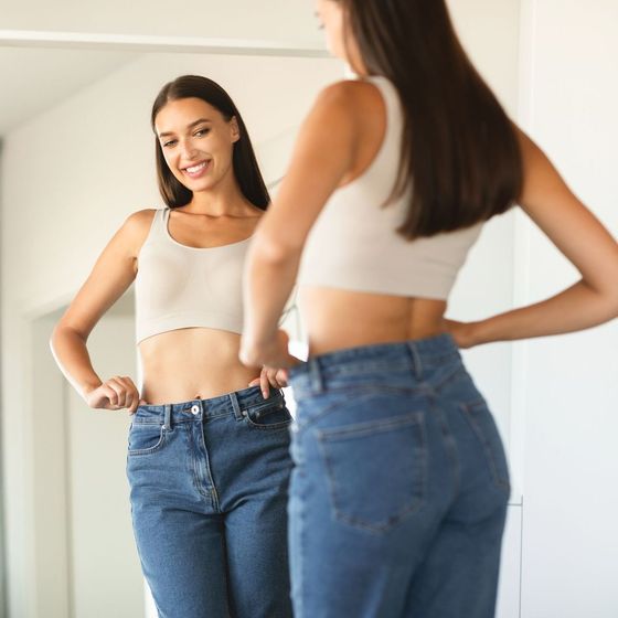 A woman in a crop top and jeans is standing in front of a mirror.