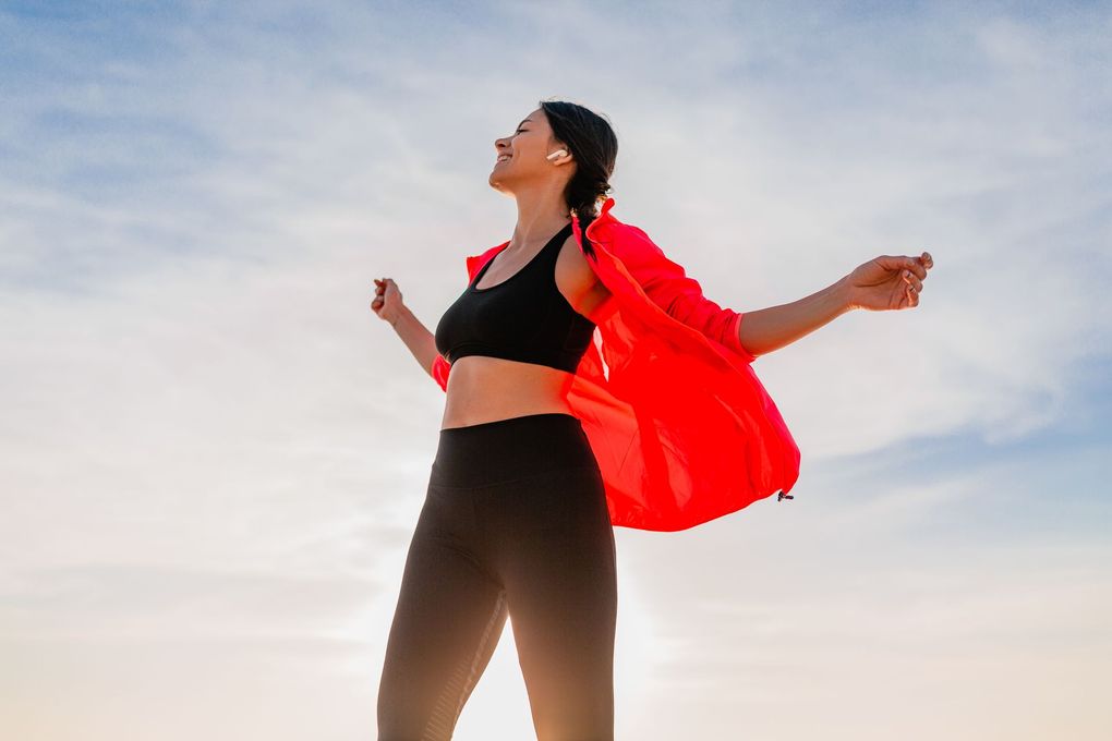 A woman in a red jacket is standing with her arms outstretched.