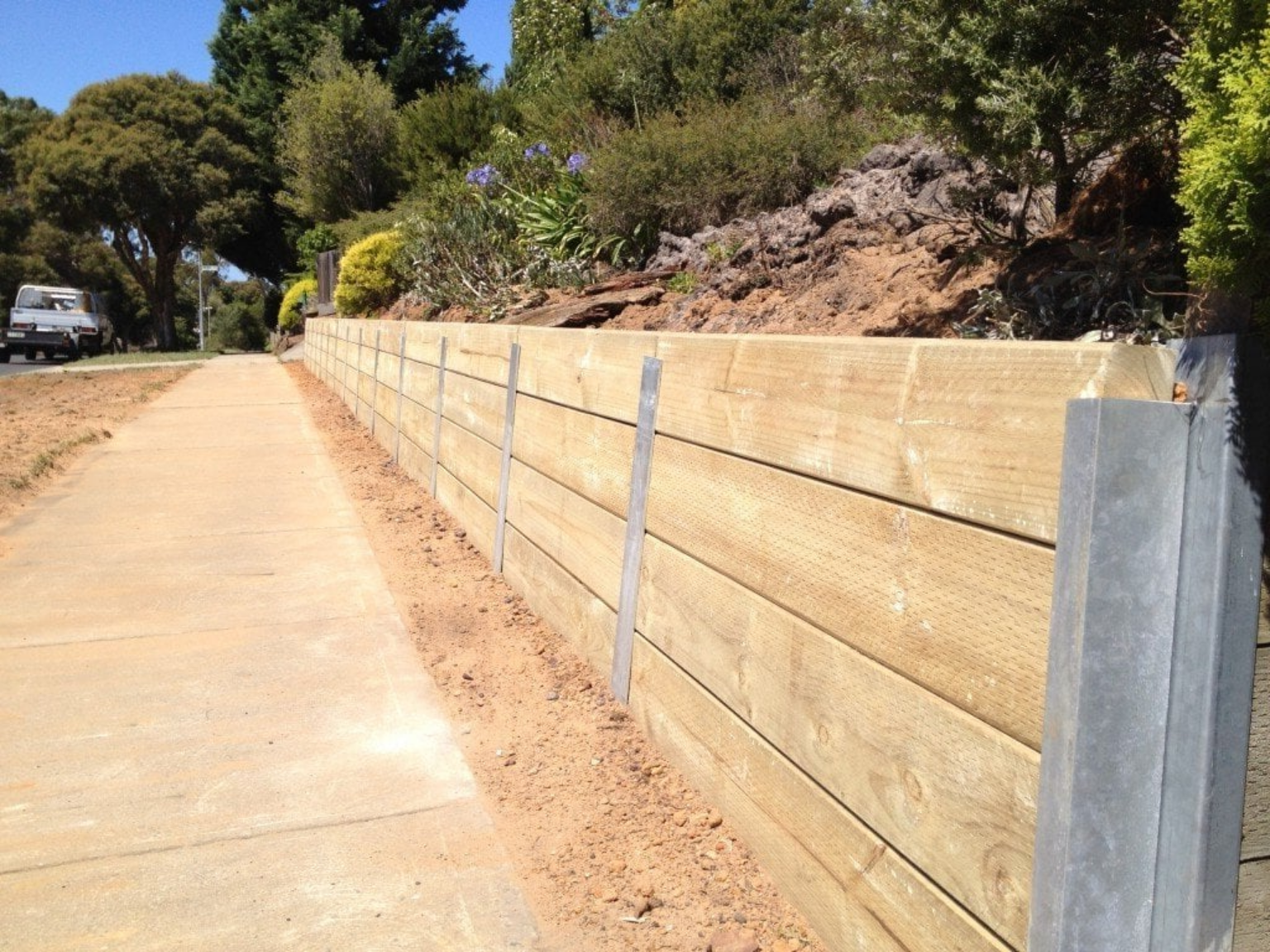 A wooden retaining wall along a sidewalk next to a road.