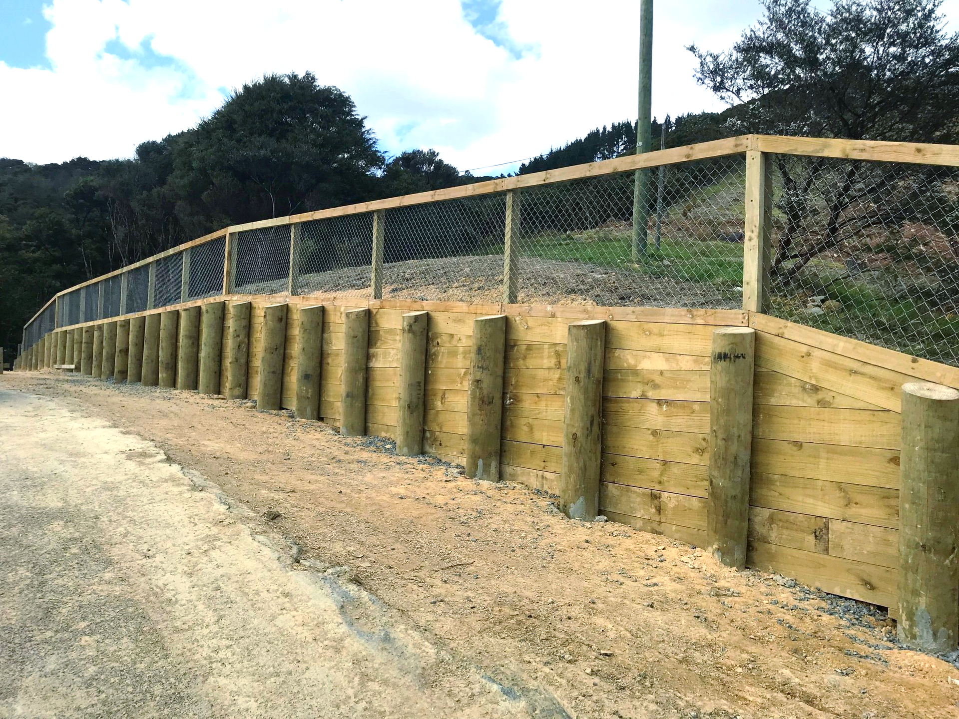A wooden fence with a chain link fence is along the side of a dirt road.