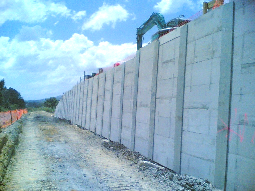 A large concrete wall is being built next to a dirt road.