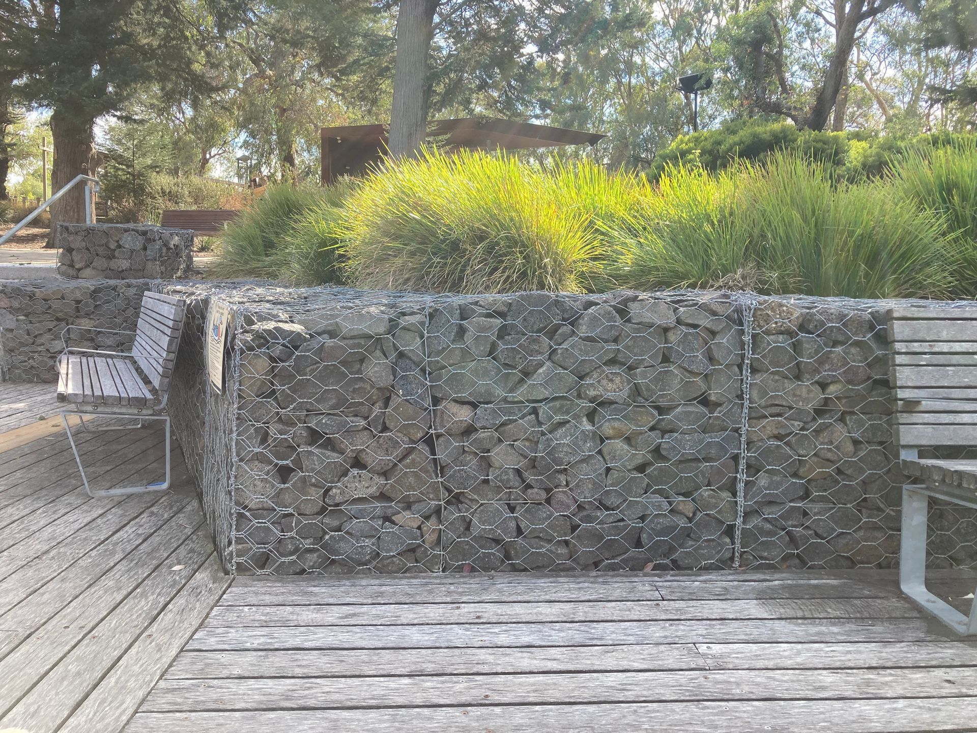A wooden deck with a stone wall and benches in the background.