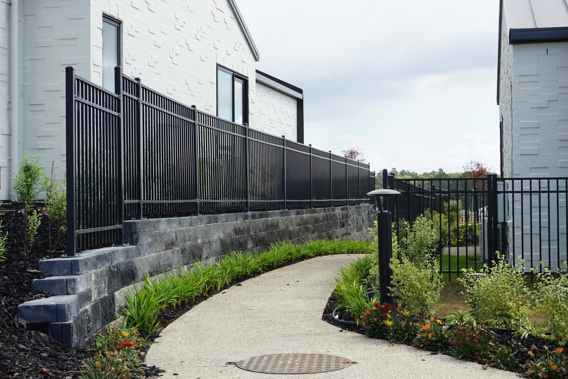 A walkway leading to a white house with a black fence.