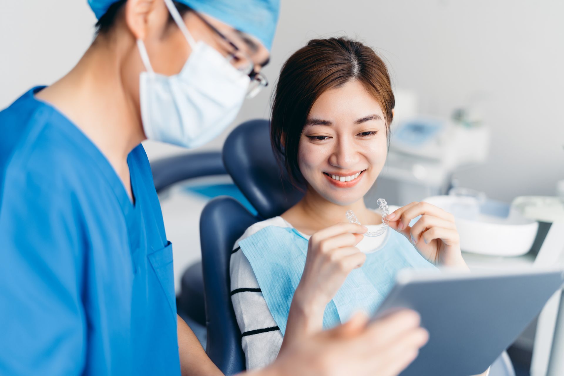 A dentist is talking to a patient in a dental chair while looking at a tablet.