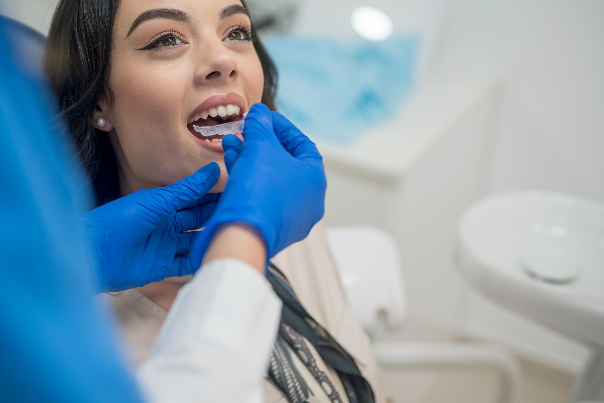 A woman is sitting in a dental chair while a dentist gently examines her teeth.